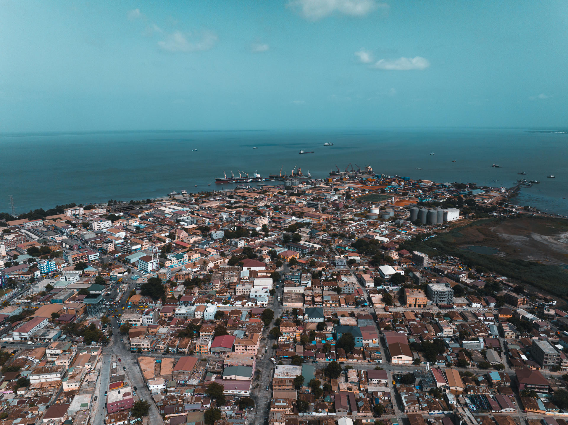 Aerial view of a coastal city with colorful buildings and a vast ocean background.