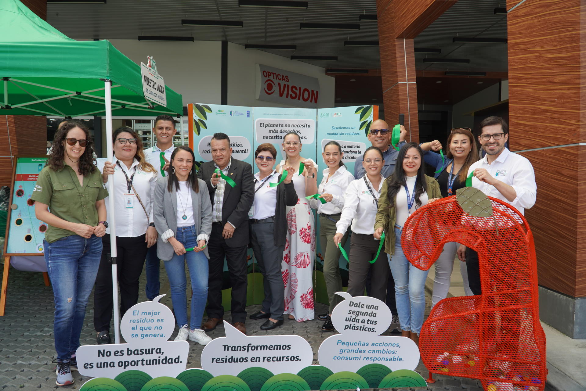 Group of people smiling and holding green ribbons at an outdoor event.