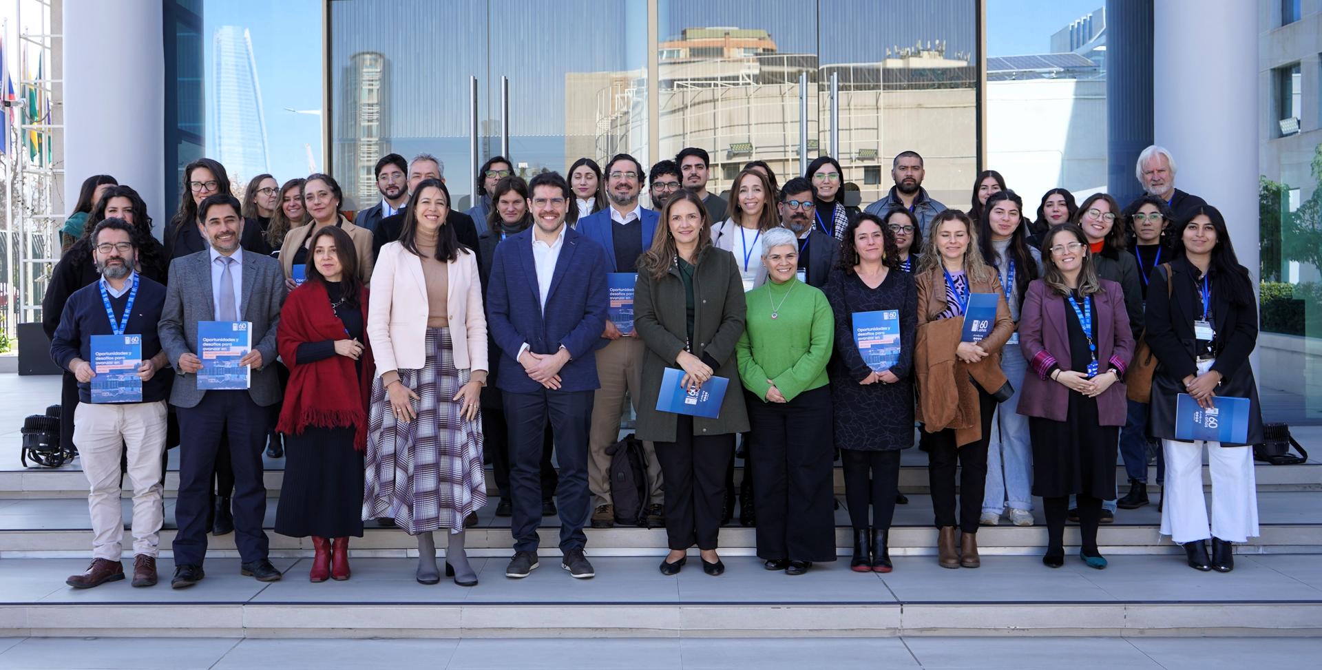 A diverse group of people posing together outside a modern building, smiling and holding documents.