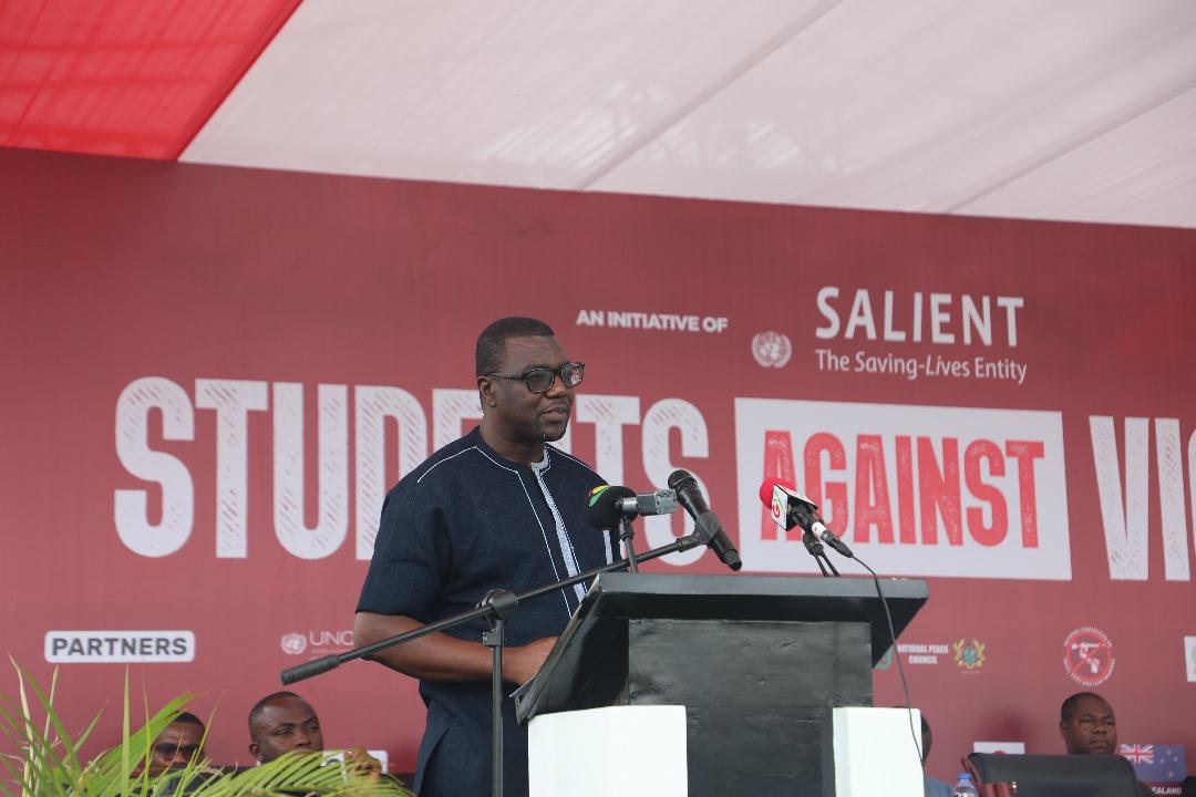 A speaker in a navy outfit addresses an audience from a podium at an event under a tent.