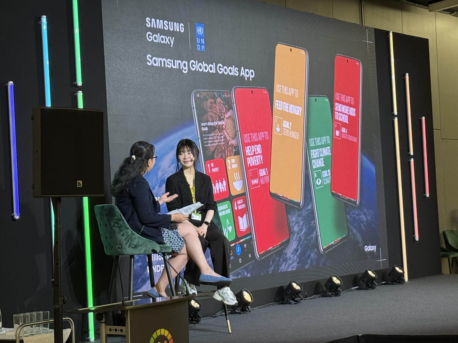 Two presenters sit on stage with colourful phone displays behind them.
