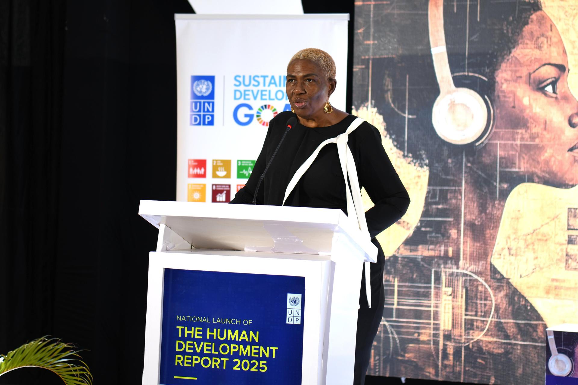 A woman speaks at a podium during a conference, with a colorful background showcasing themes of development.