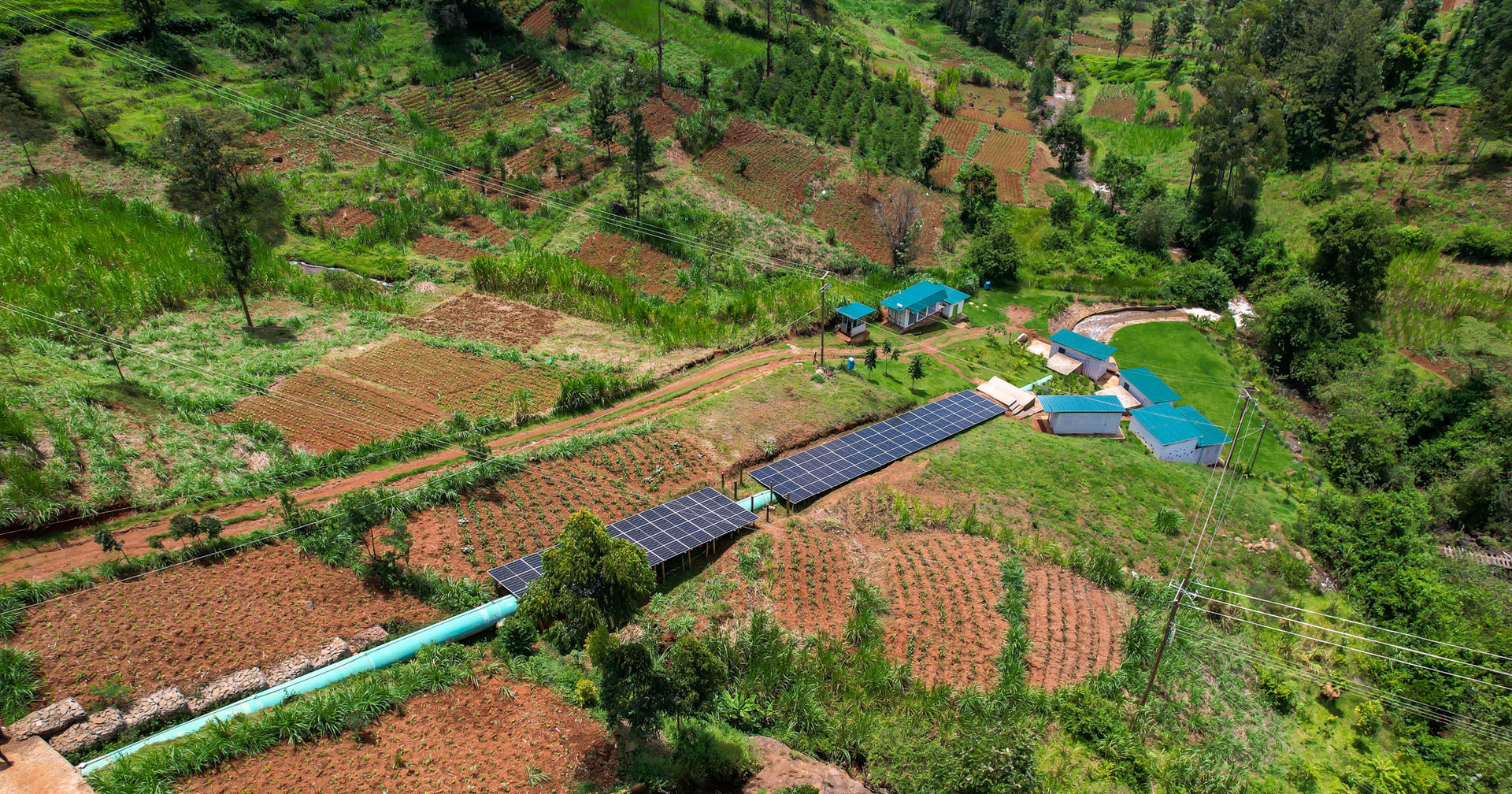Aerial view of a rural landscape with solar panels, gardens, and scattered buildings.