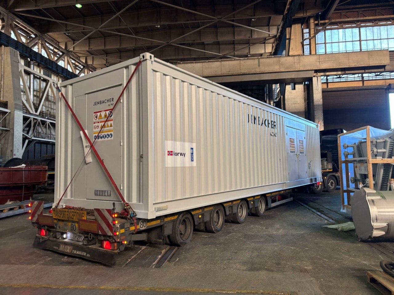 Shipping container on a trailer inside a warehouse, with industrial surroundings.