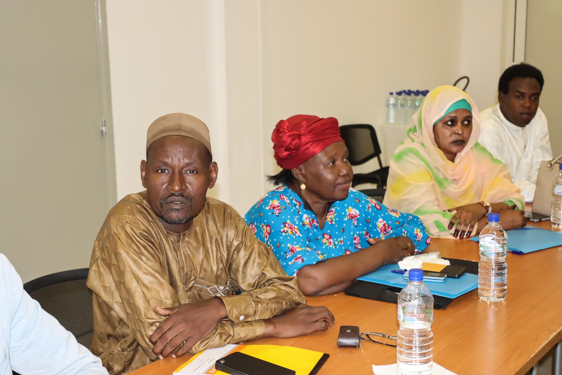 A diverse group of four people seated at a table, engaged in discussion, with water bottles and notebooks.