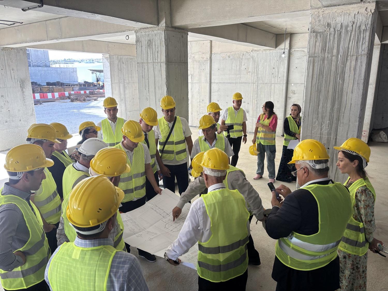 Group of people in hard hats and vests discussing plans at a construction site.