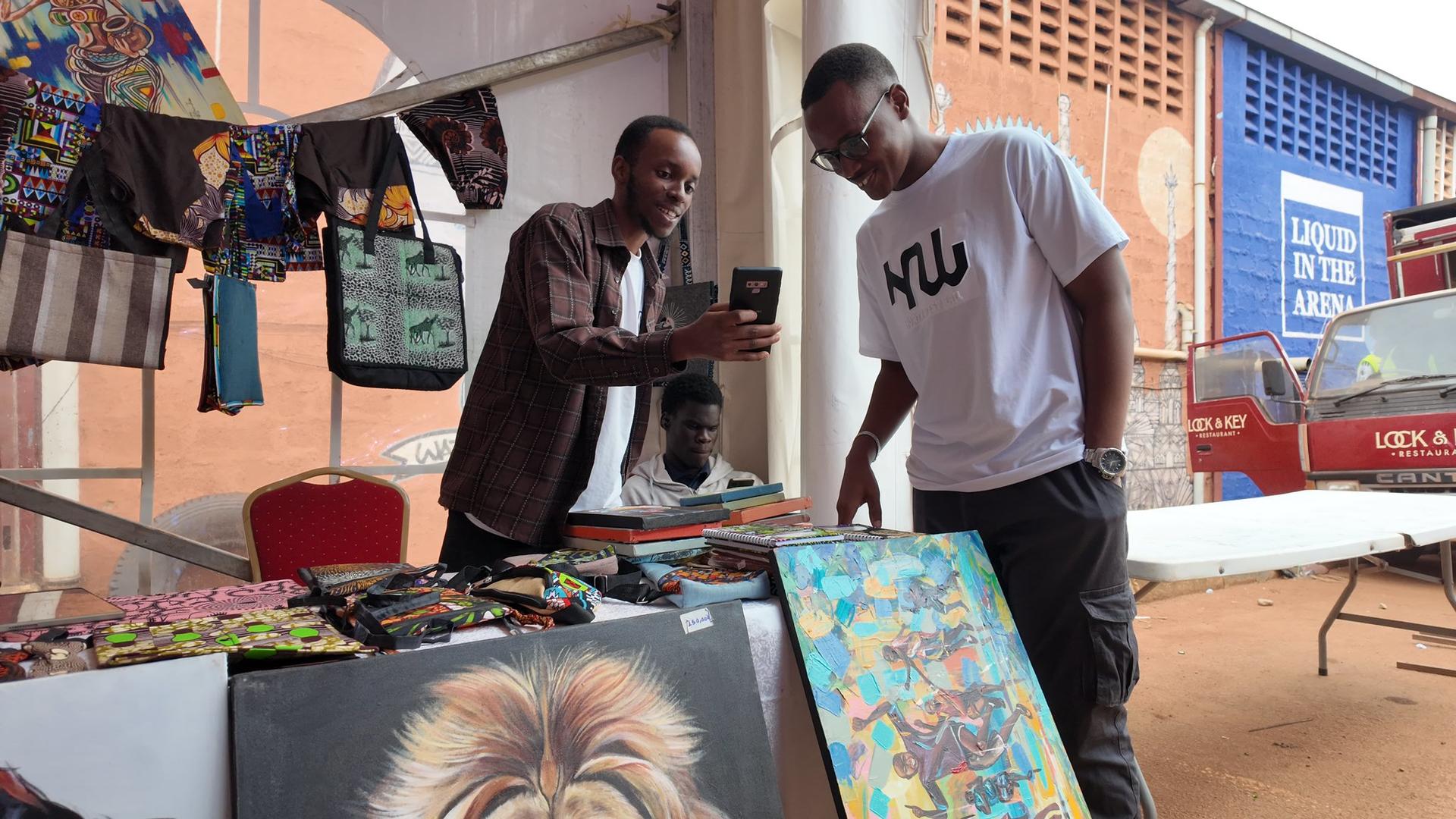 Two men engage while examining colorful artwork at a market stall.