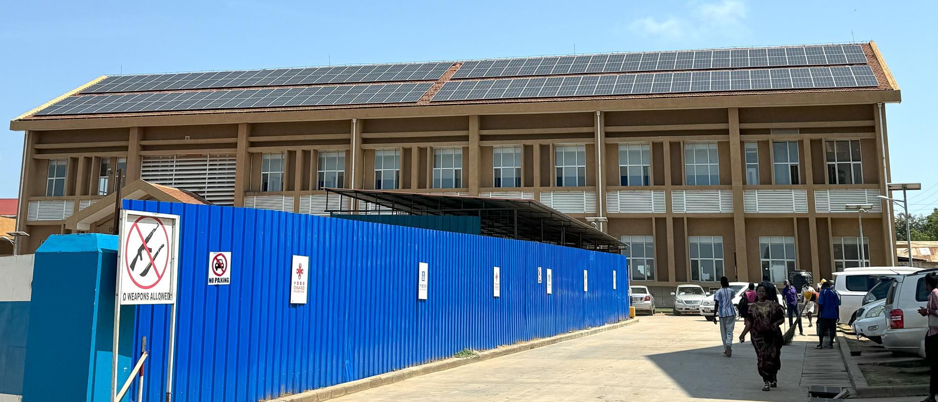 Modern building with solar panels, surrounded by construction barriers and people walking.