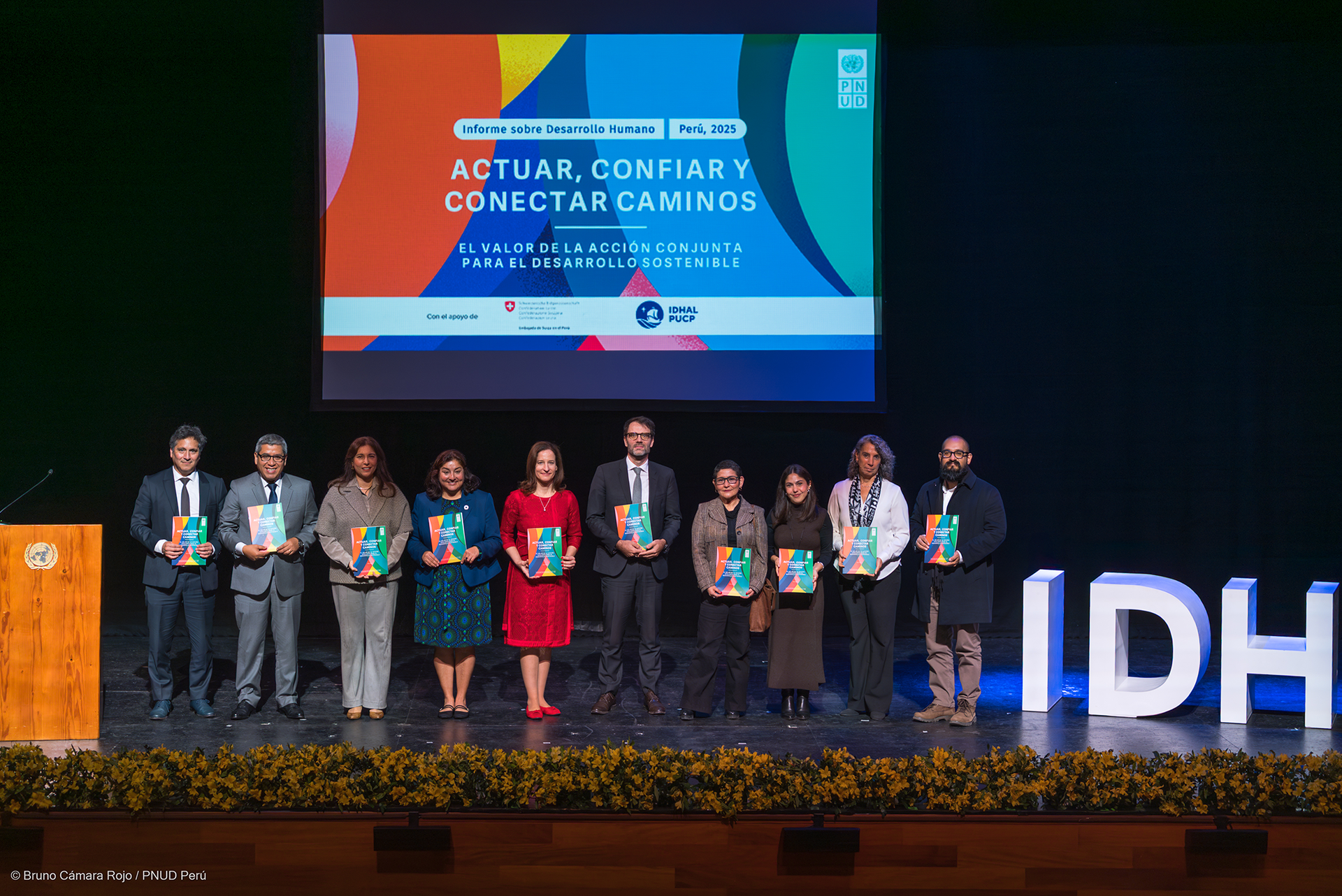 A group of people stands in front of a large screen holding awards on a stage.