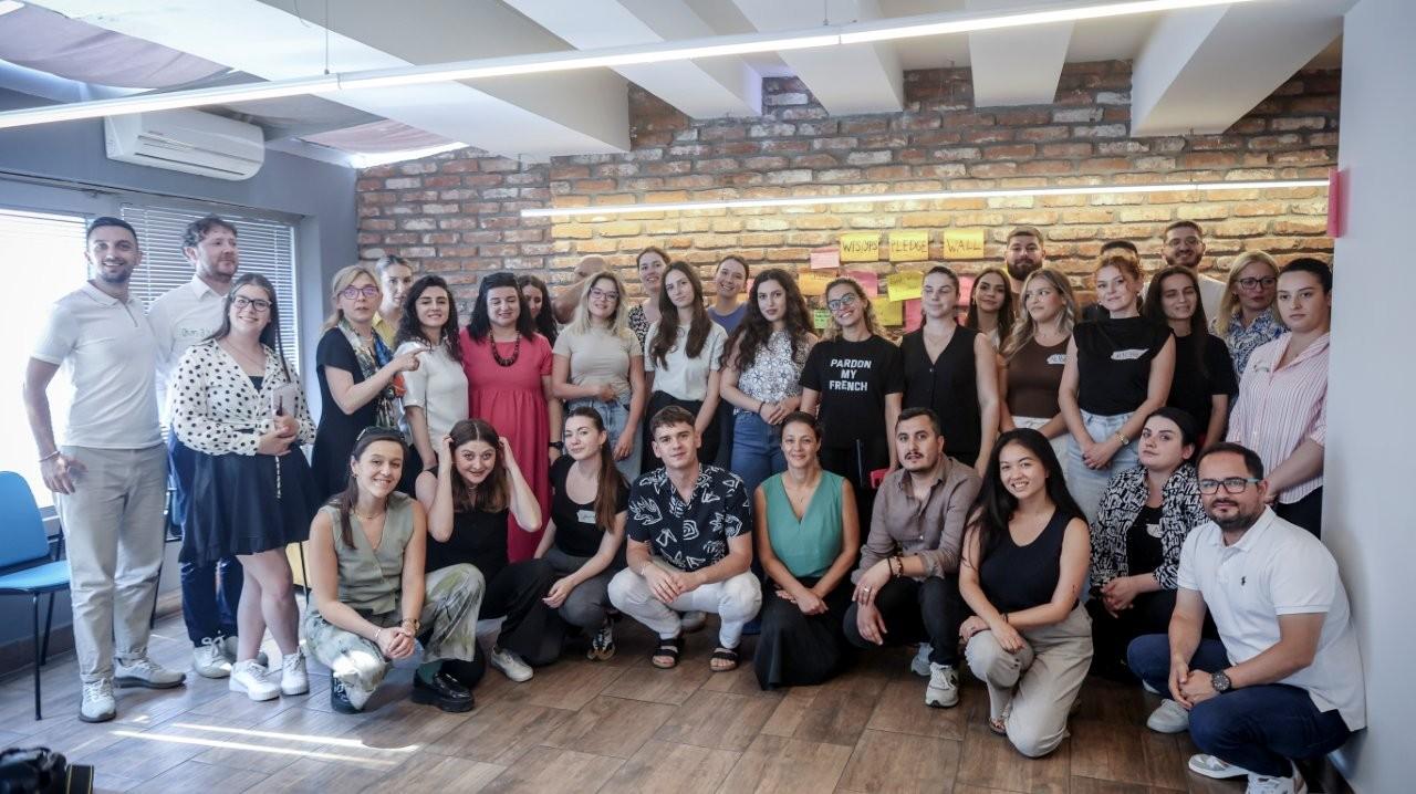 A group photo of approximately 30 people in a modern room with a brick wall.