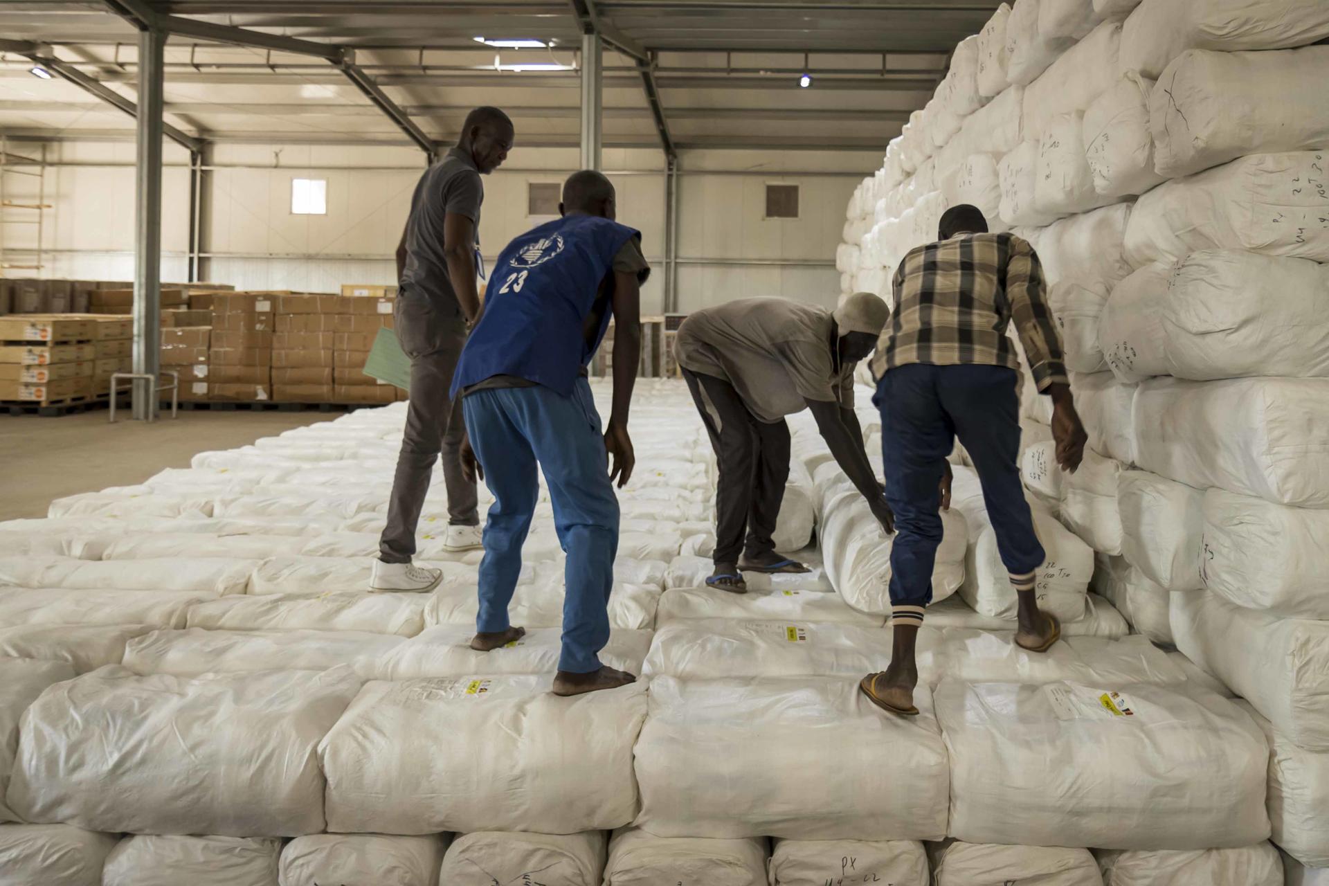 Workers stacking large bundles of white material in a warehouse.