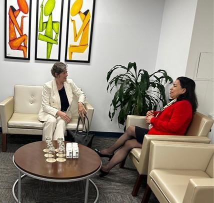 Two women sitting in chairs, engaged in conversation, surrounded by colorful artwork and a plant.