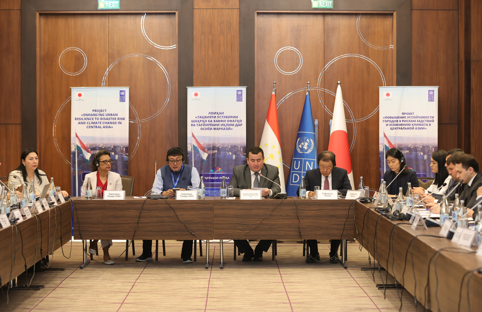 A panel discussion with speakers seated at a long table, flags and banners in the background.