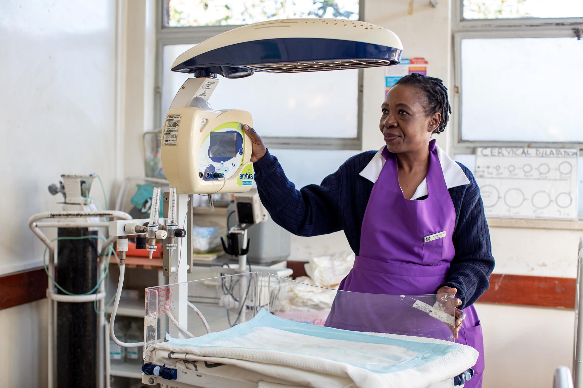A nurse in a purple apron operates a medical device in a bright clinic room.