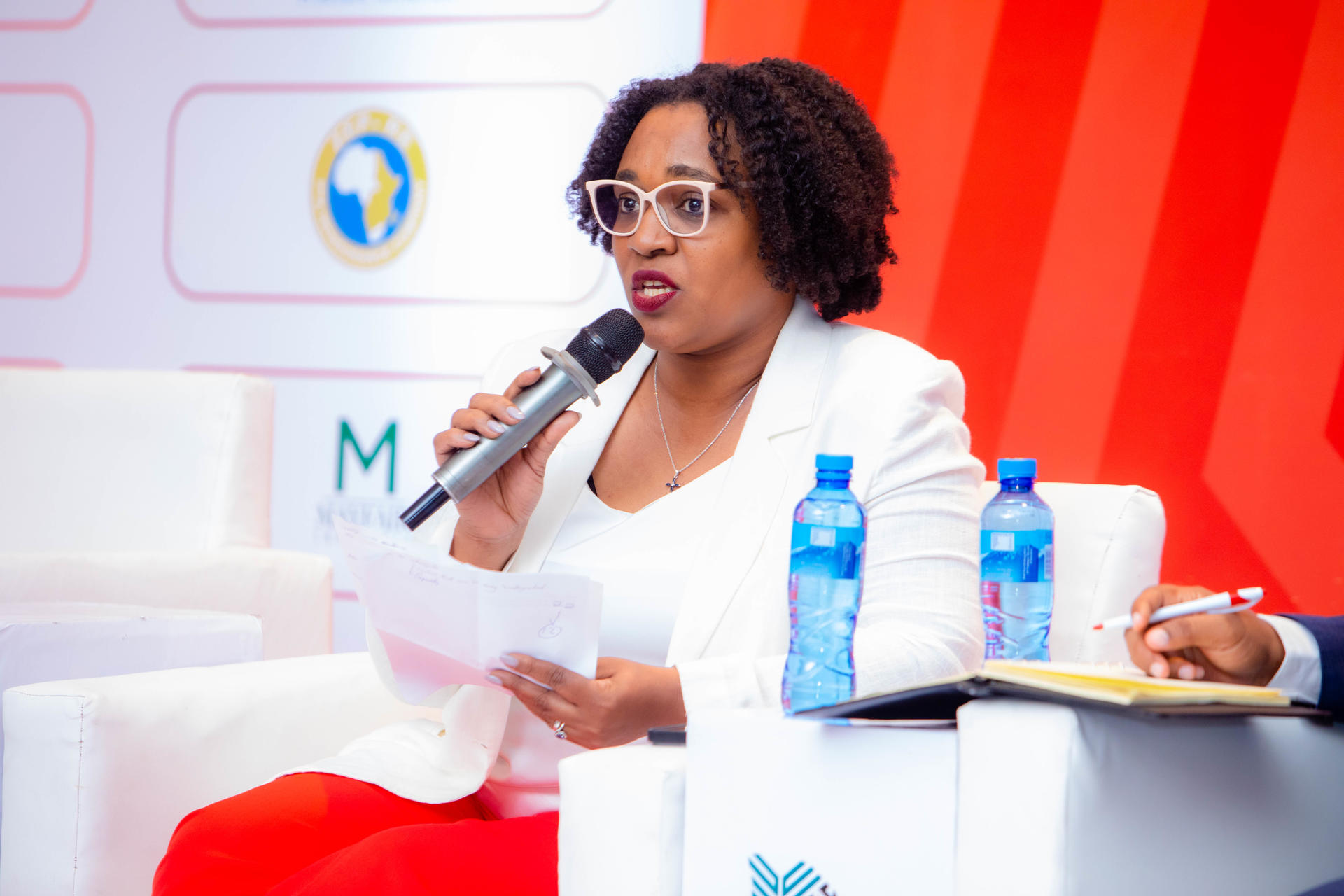 A woman with curly hair speaks into a microphone at a panel discussion.