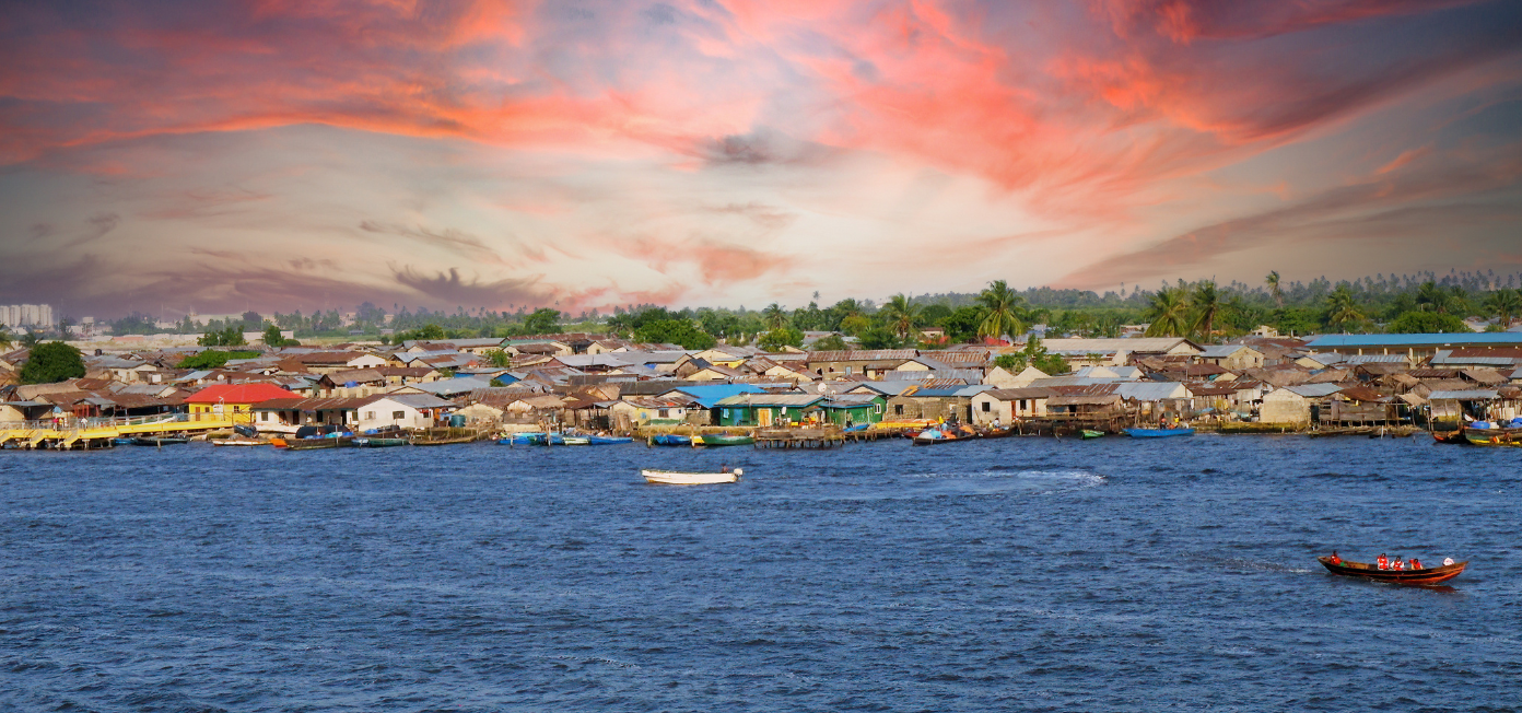 Colorful houses line a waterfront under a vibrant sunset sky with boats on the water.