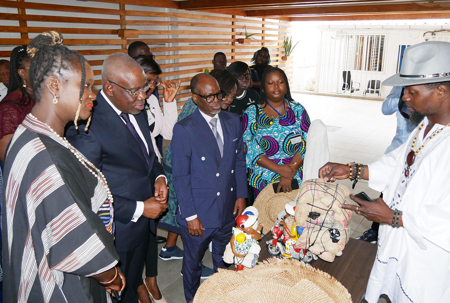 A group of people observes an artisan showcasing traditional crafts in a bright indoor setting.