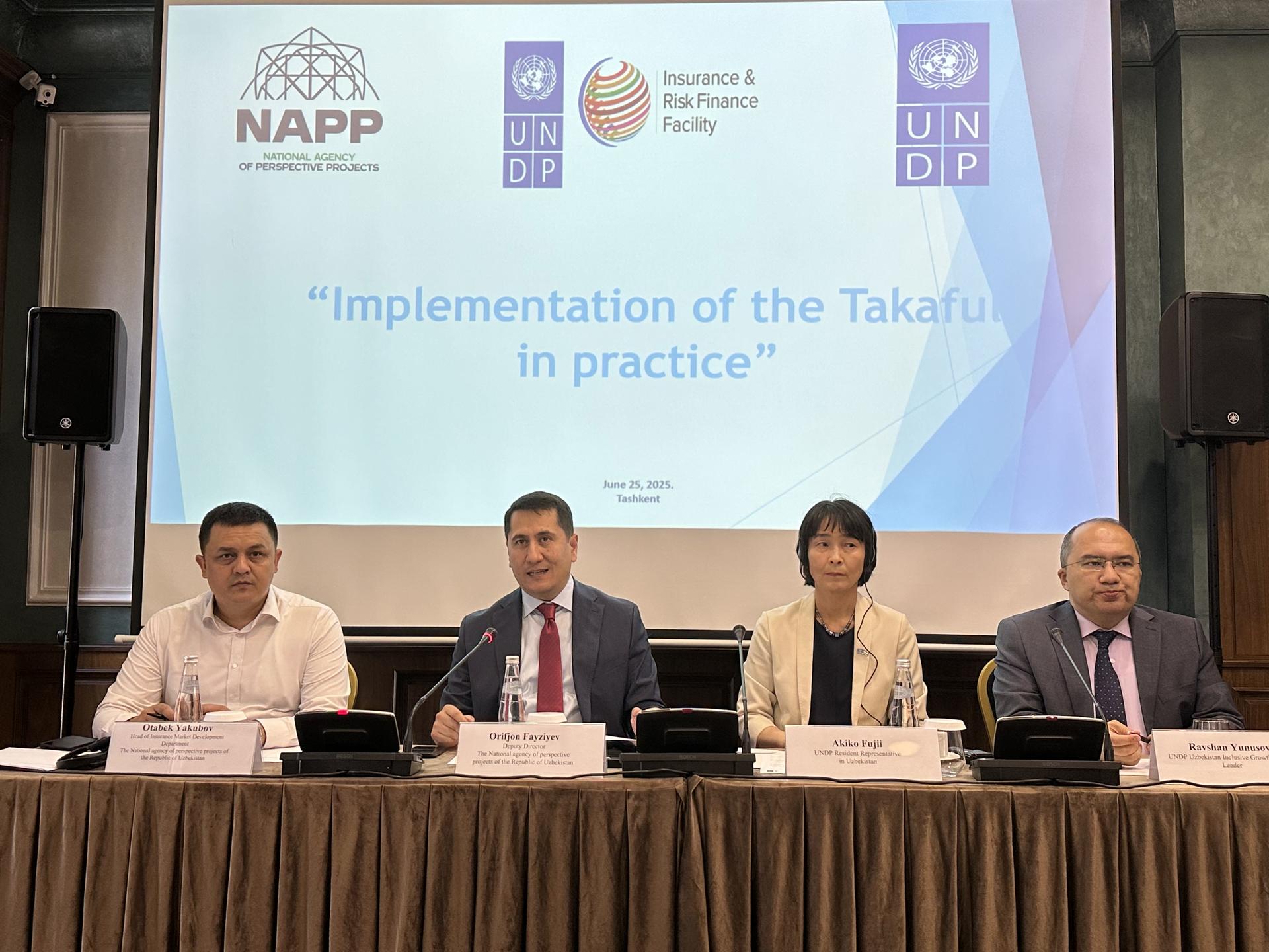 Four panelists sit at a table during a conference, with branding and presentation slides in the background.