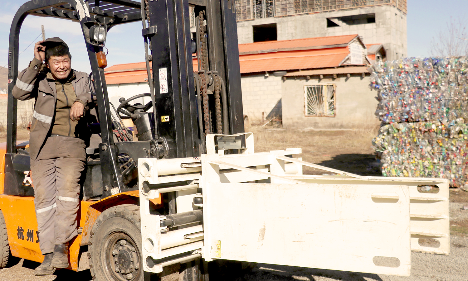 Worker smiling while operating a forklift near a building and a stack of materials.