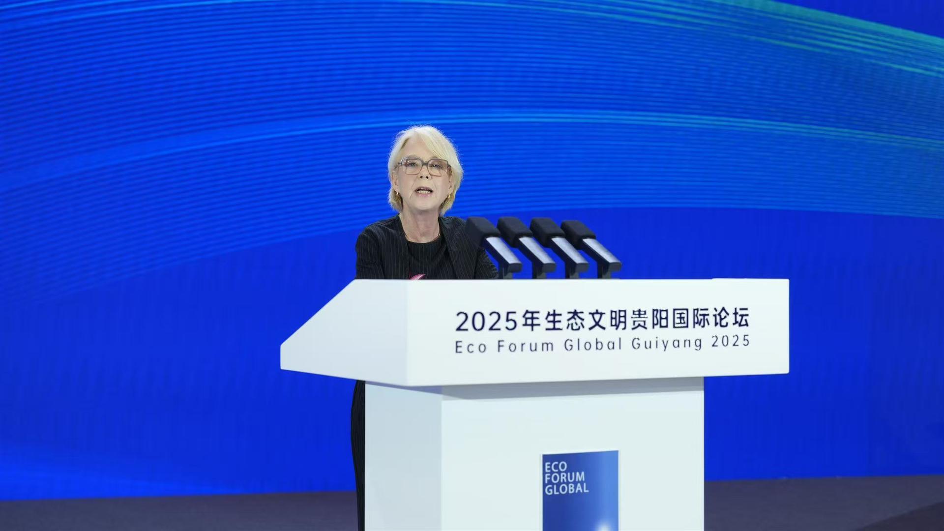 A woman speaking at a podium during a conference, with a blue background.