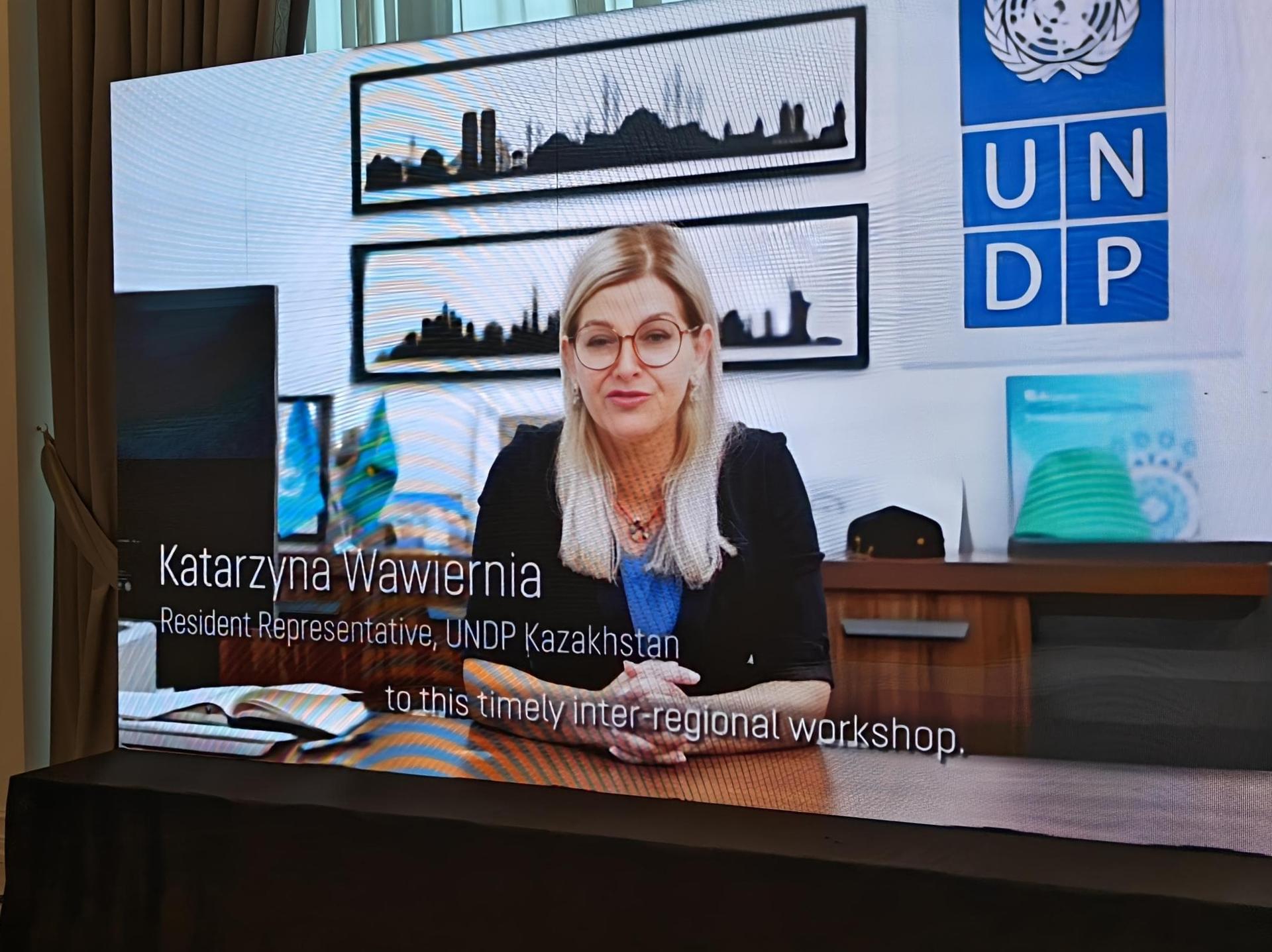 A woman with glasses sits at a desk, speaking during a workshop presentation.