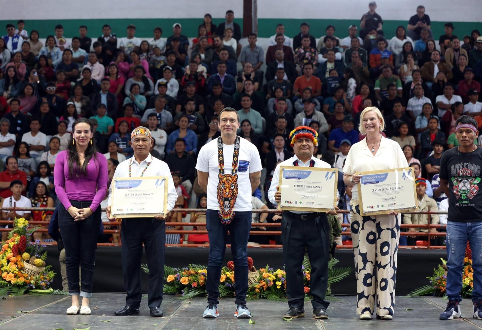 Five individuals standing on a stage, holding certificates, with a large audience seated behind them.