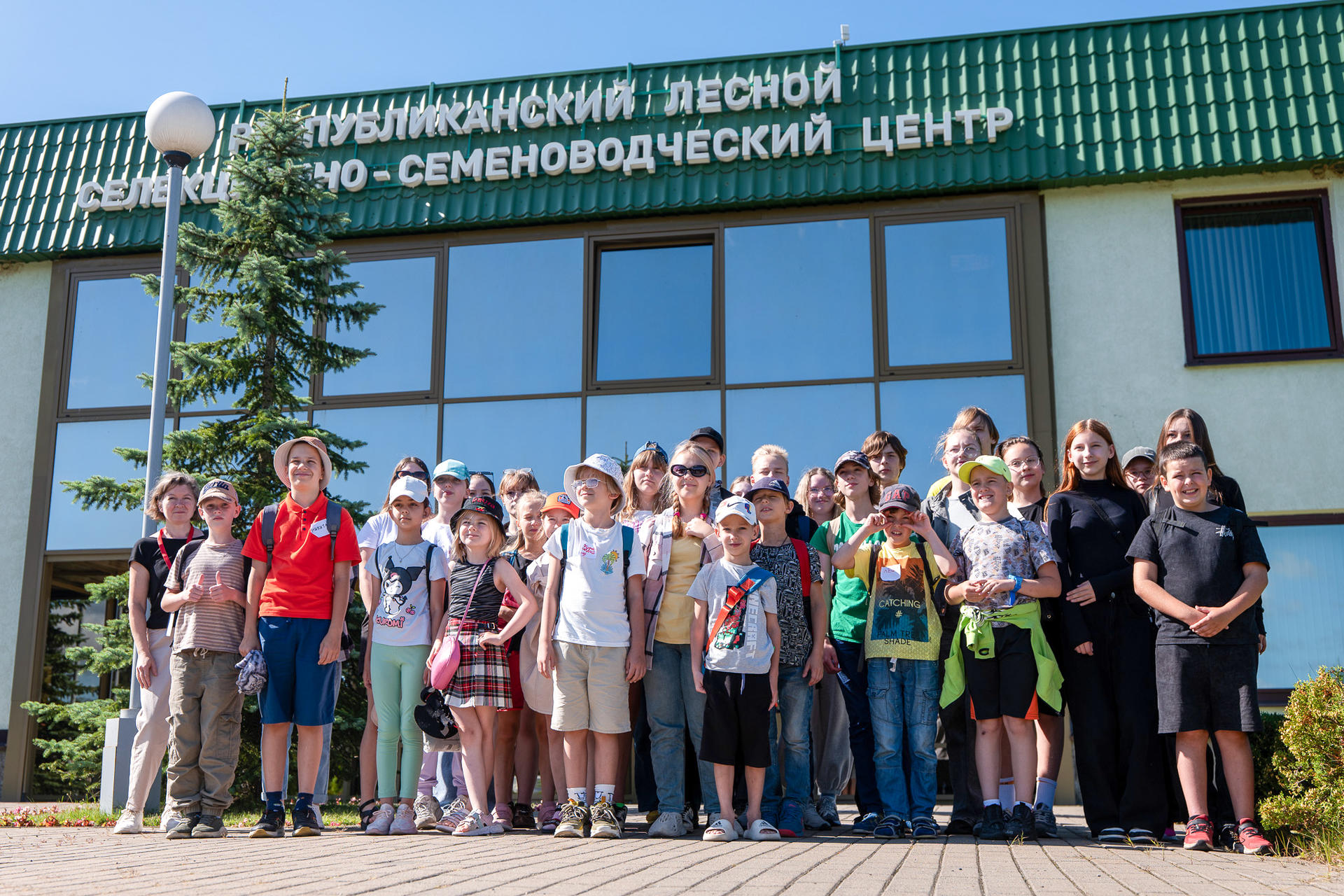 Большая группа детей и взрослых позирует перед зданием центра в солнечный день.