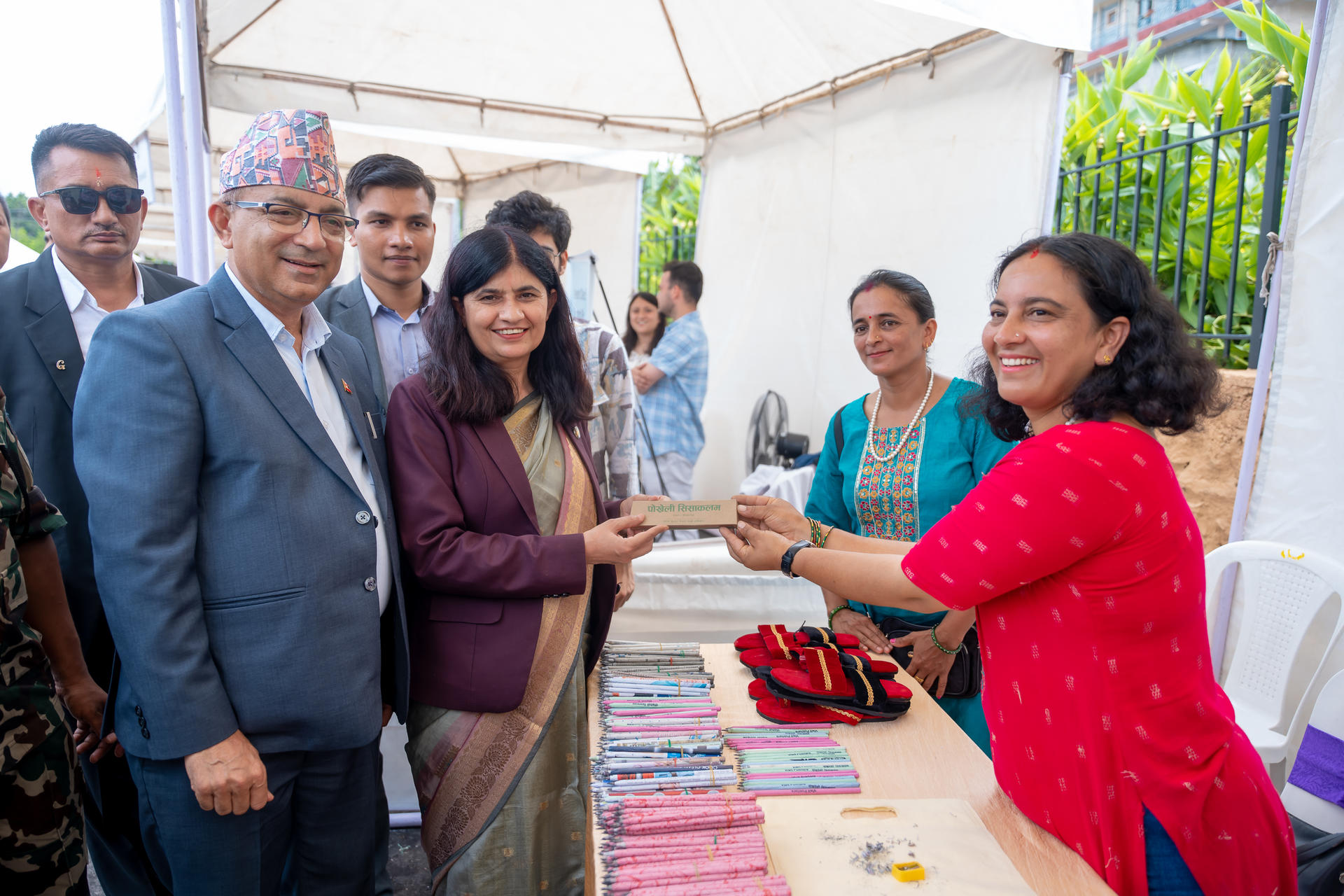 A group of people interacting at a stall, exchanging items with smiles in a outdoor setting.