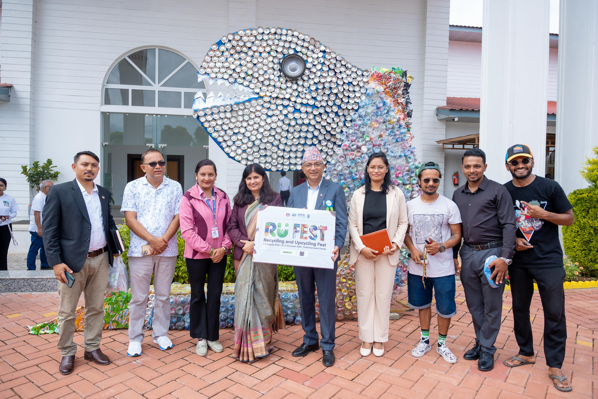 A group of people posing in front of a colorful fish sculpture at an event.