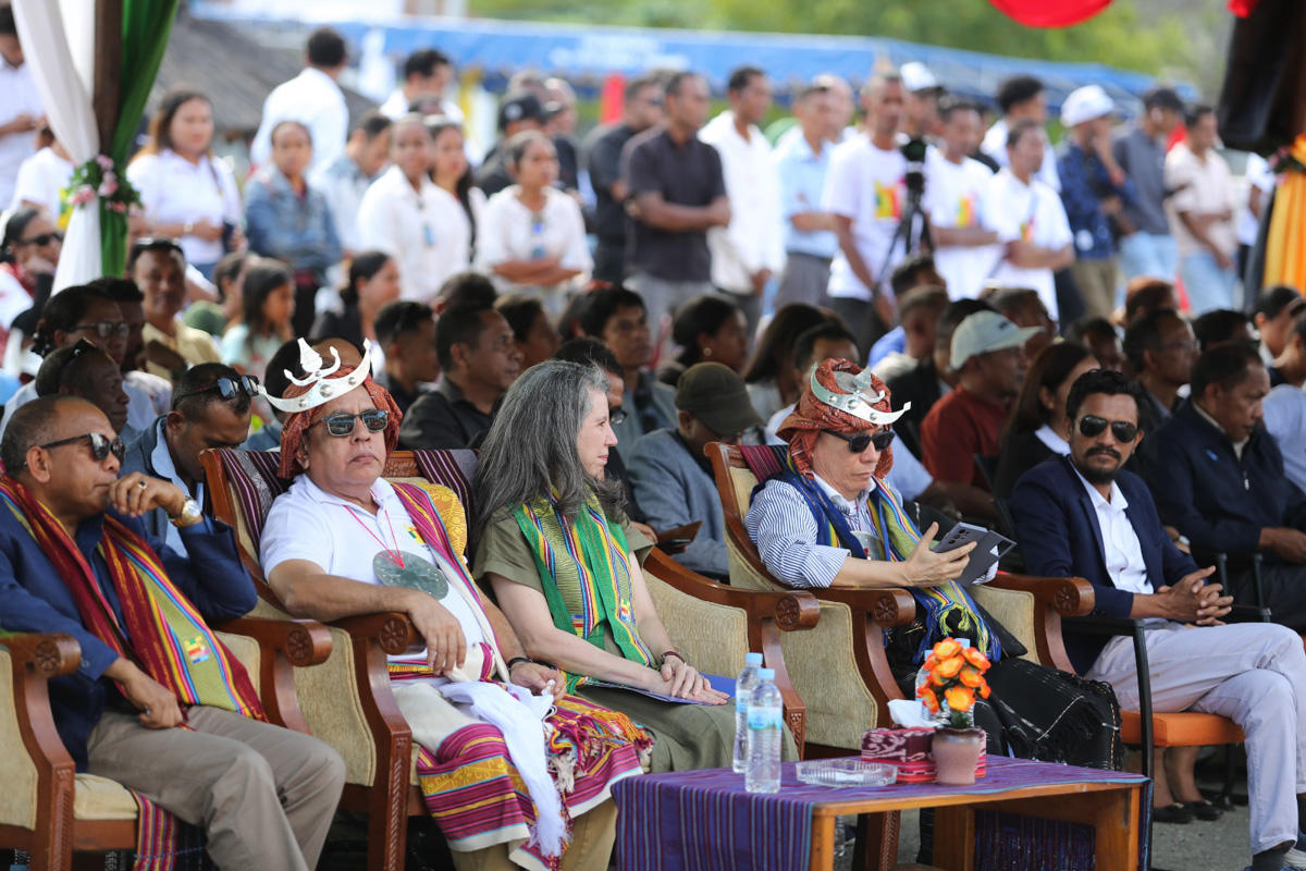 A diverse group of people seated in a crowded outdoor setting, some wearing traditional attire.