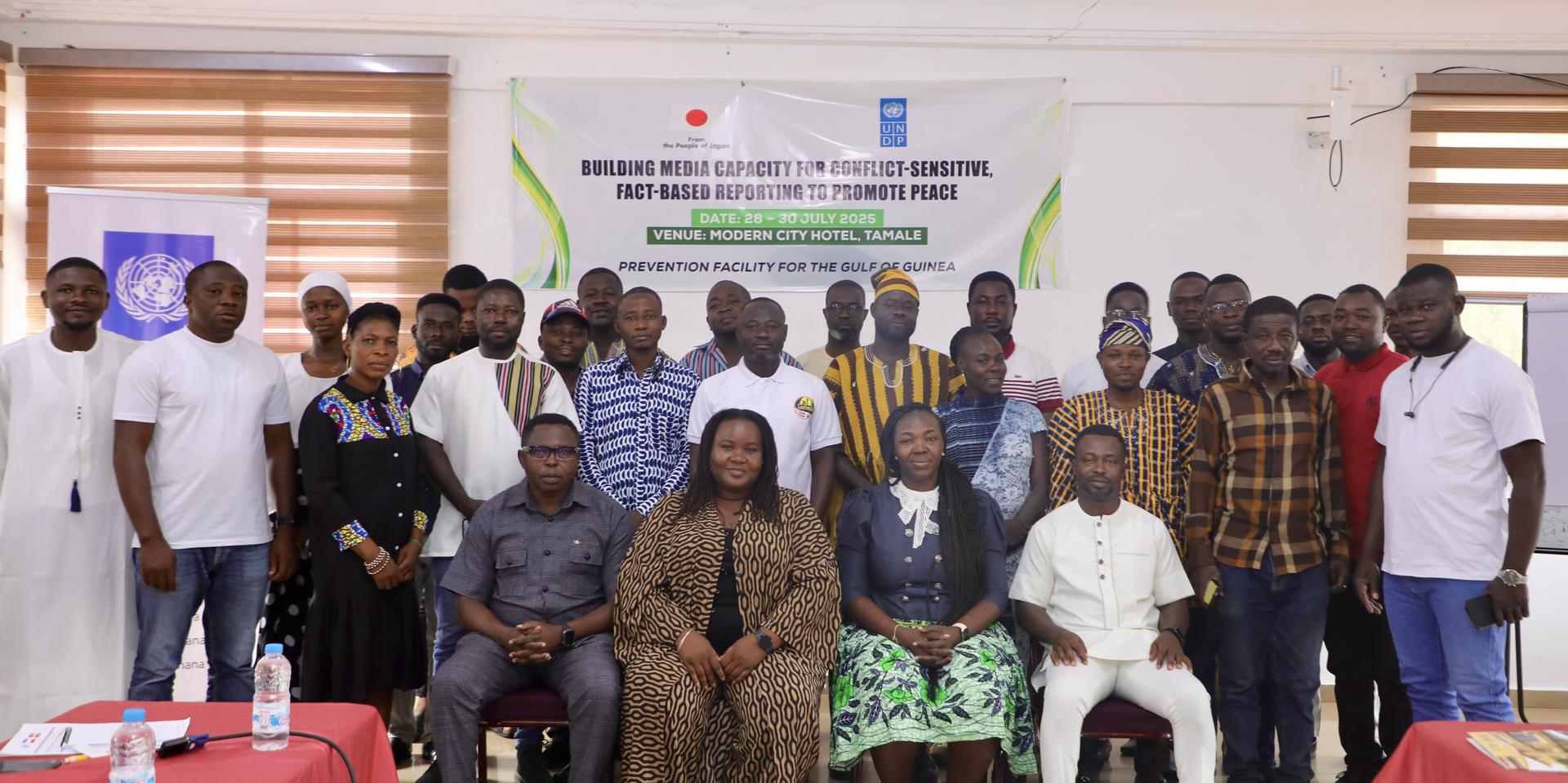 Group photo of participants and speakers at a seminar, seated and standing, in a bright room.