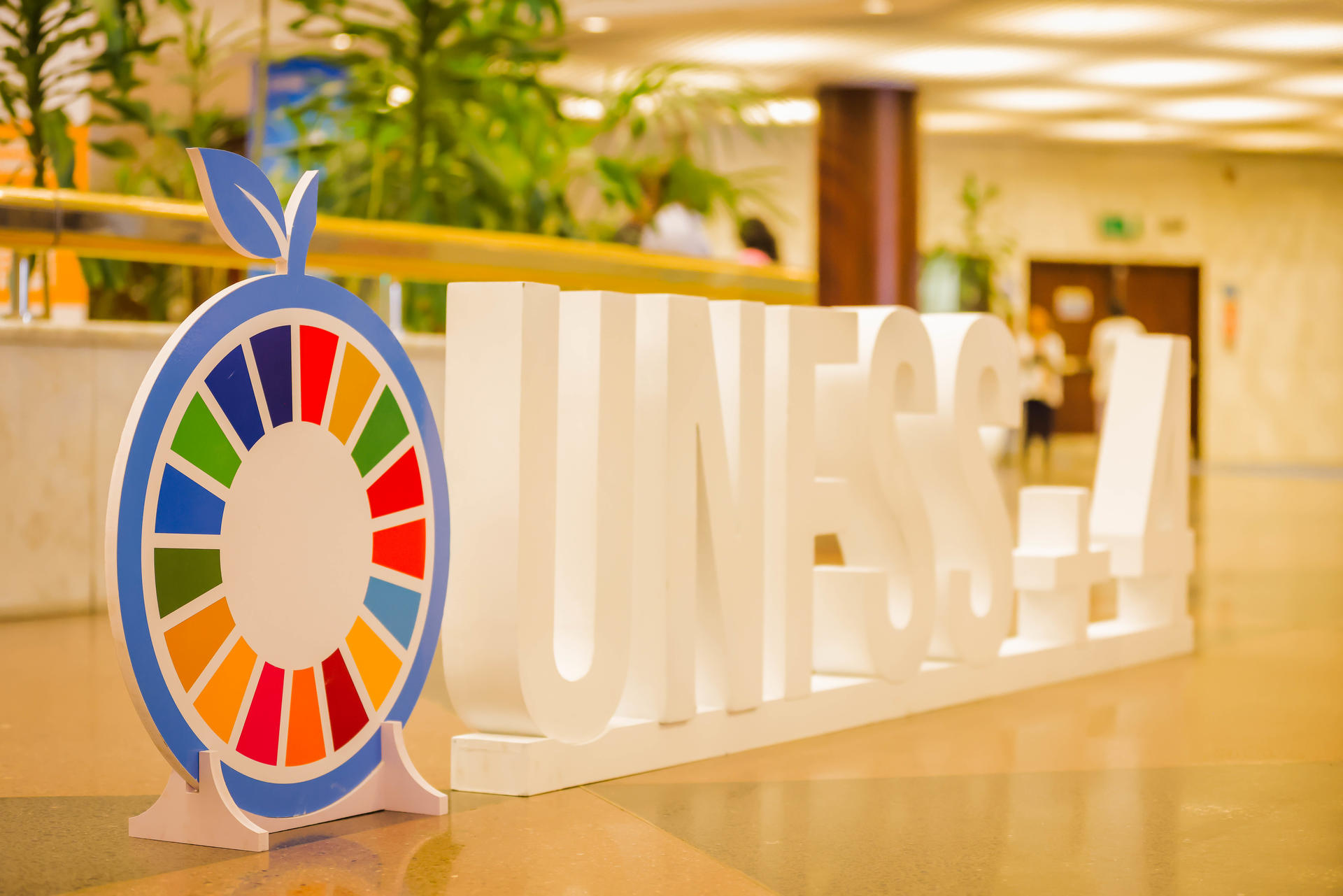 Colorful logo of the Sustainable Development Goals beside "UNESS" in a bright, indoor setting.