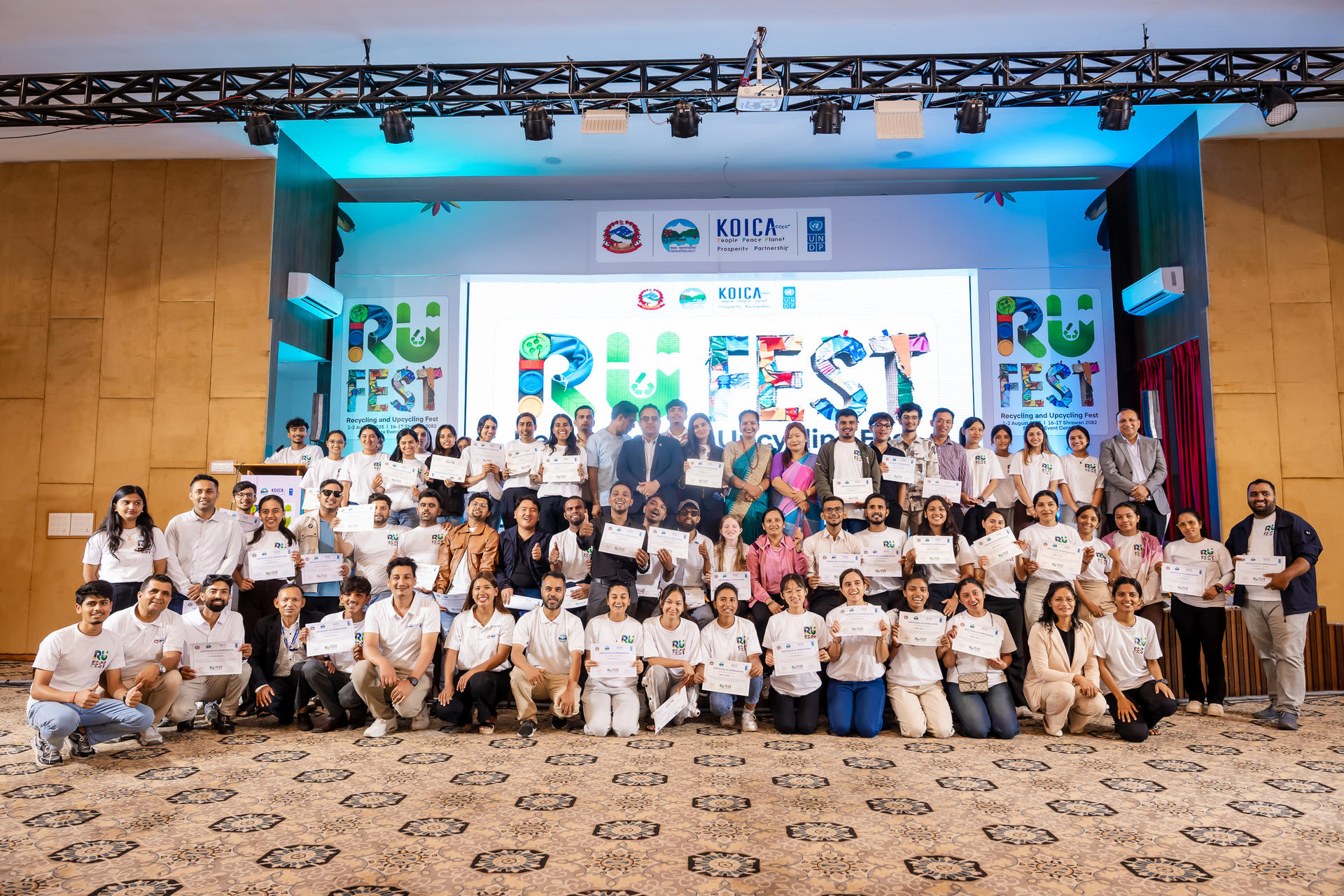 Group photo of participants at an event, posing together on stage with colorful banners.