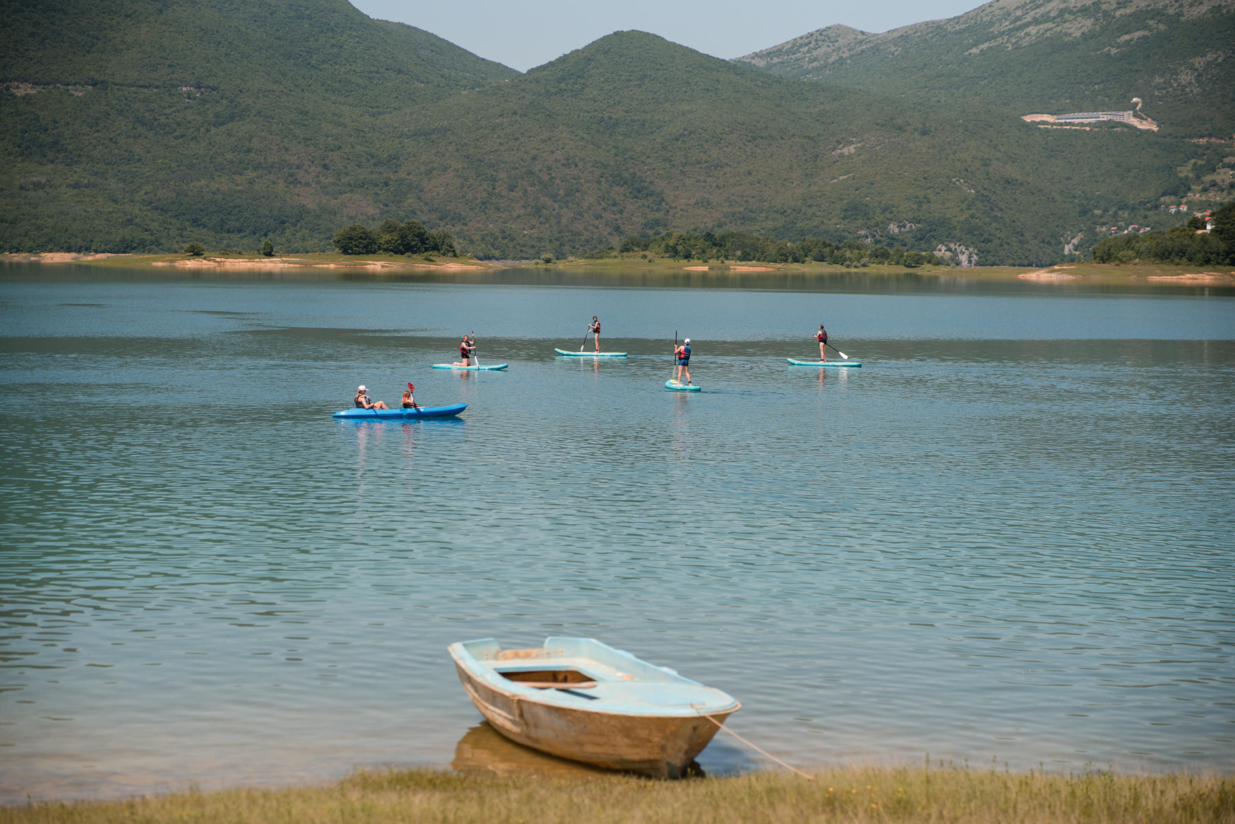 A calm lake with a small boat in the foreground and people kayaking in the distance.