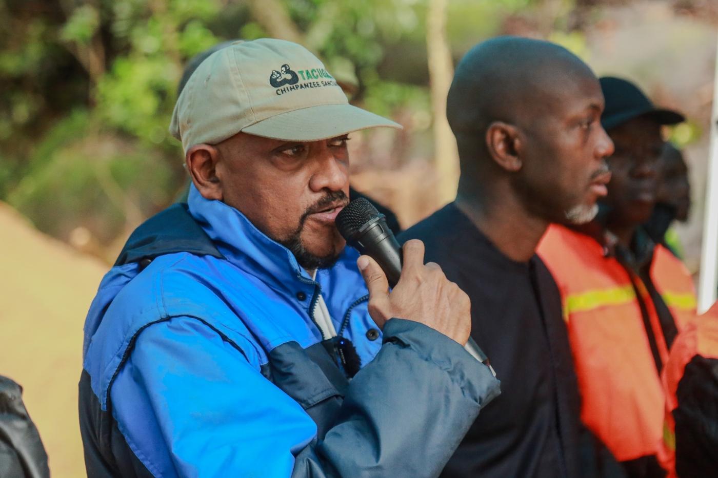 A man in a blue jacket holds a microphone, speaking while others listen attentively.