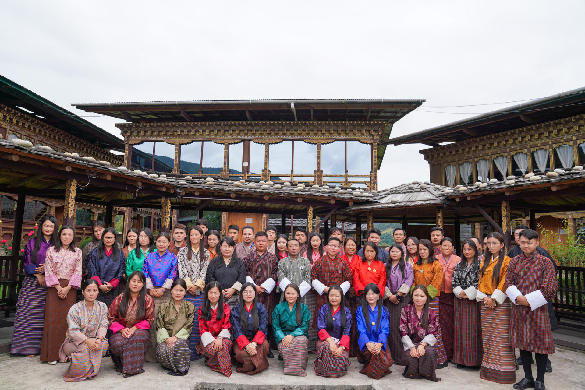 A large group of people dressed in colorful traditional attire pose together outdoors.
