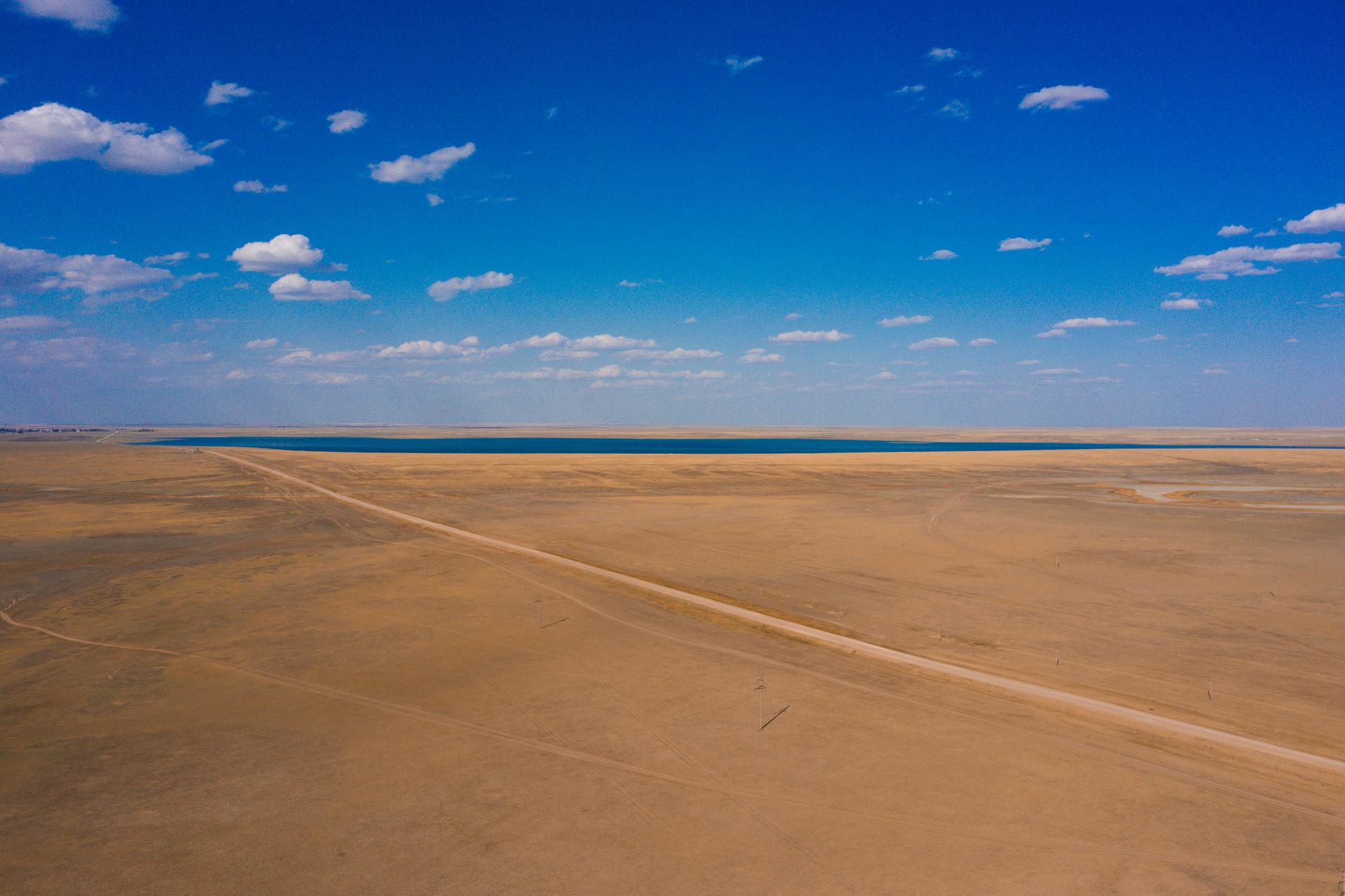 A vast desert landscape with a clear blue sky and a distant body of water.