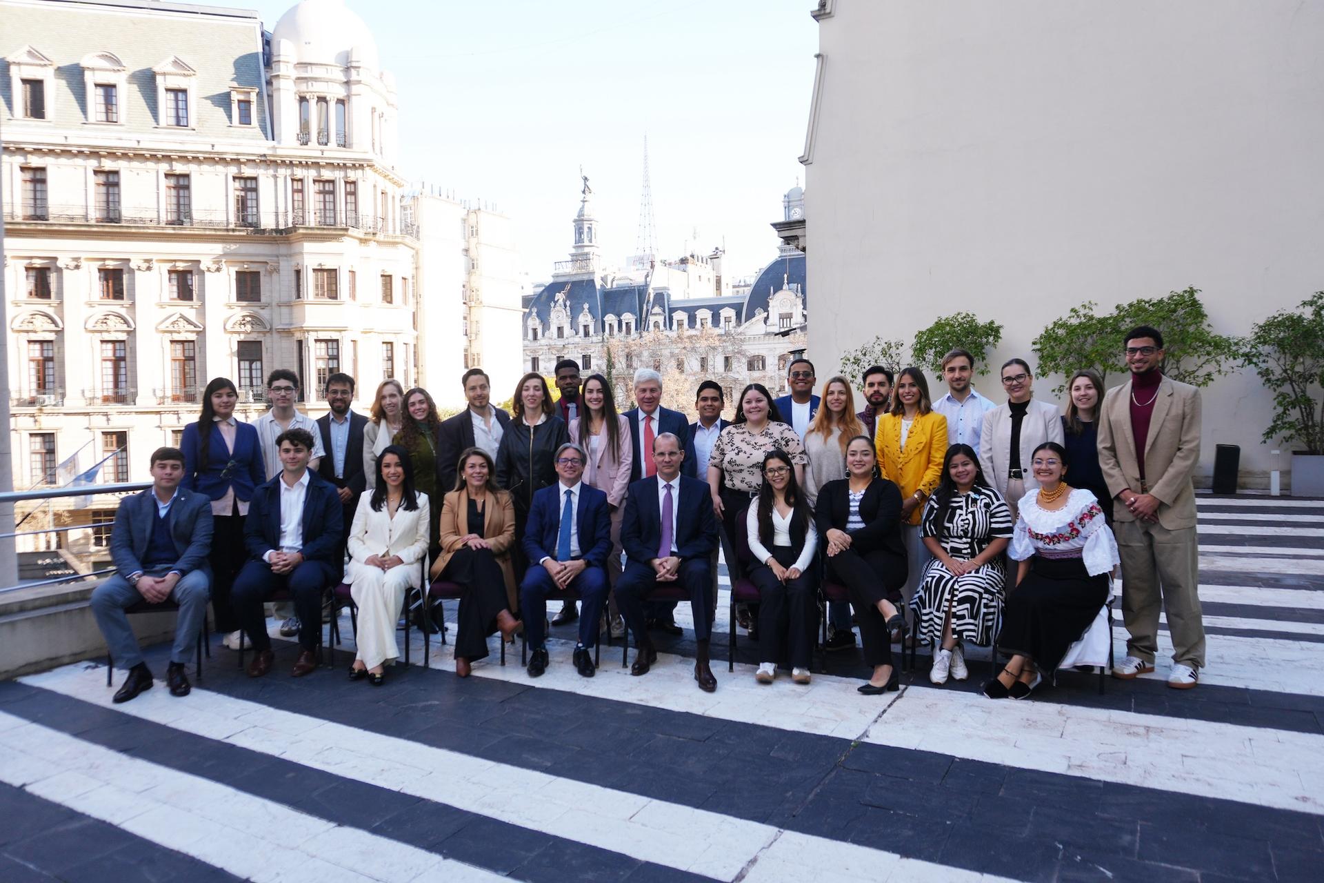 Group photo of diverse individuals in formal attire, posed outdoors in front of a cityscape.