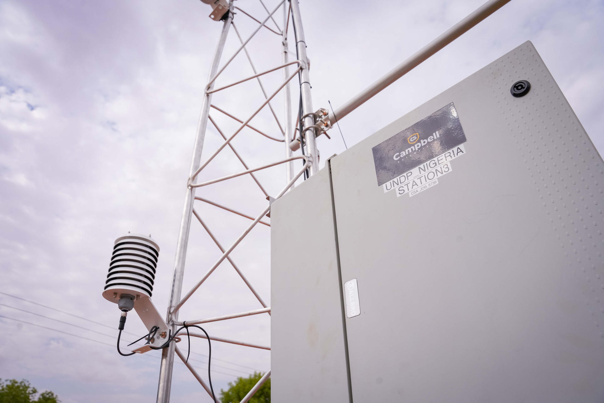 Communication tower with a control box and an anemometer under a cloudy sky.