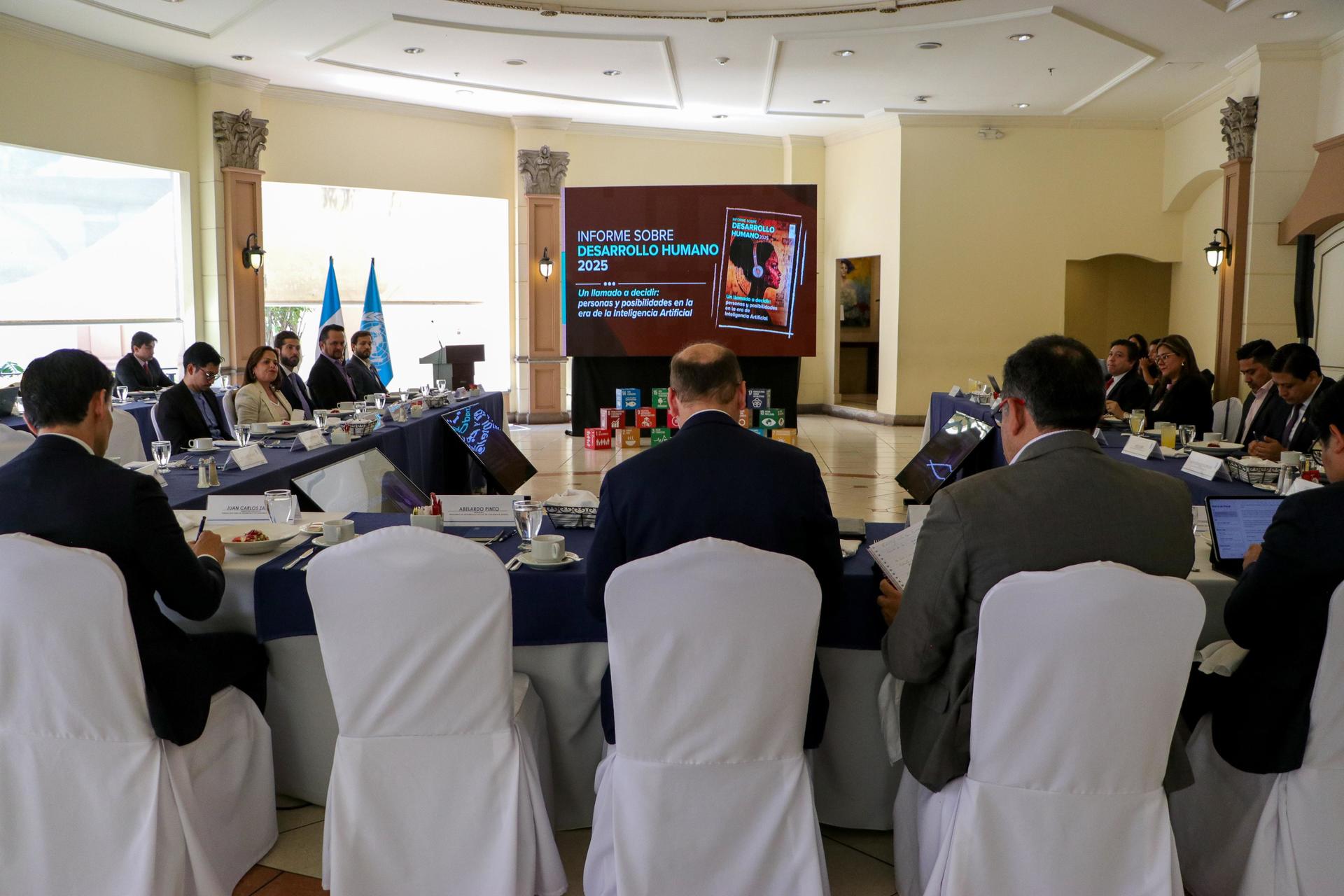 A meeting with participants seated around a table, facing a presentation screen.