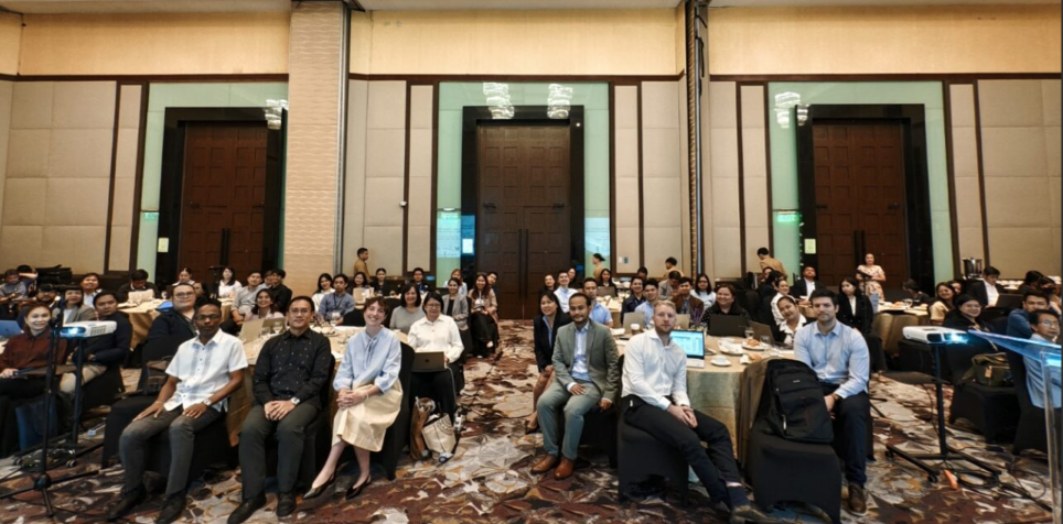 A large audience seated in a conference room, focused on a presentation.