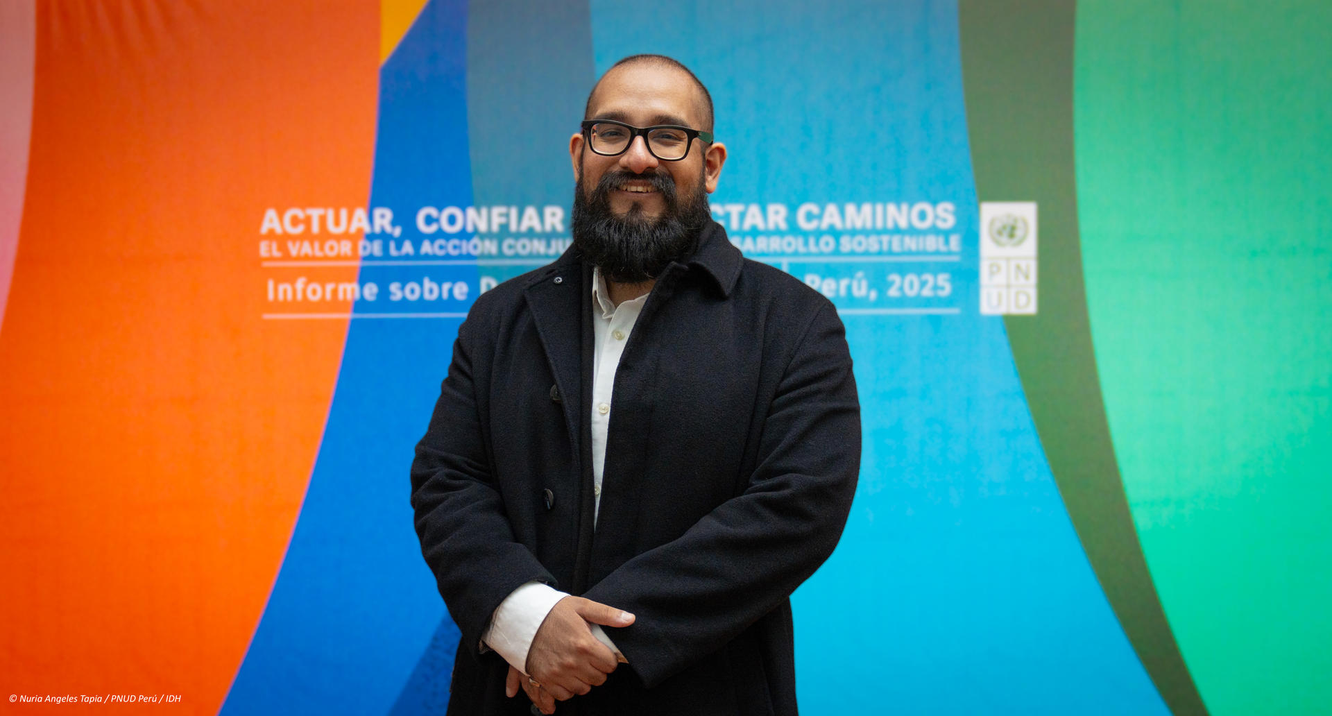 A man with a beard stands confidently in front of a colorful abstract background.
