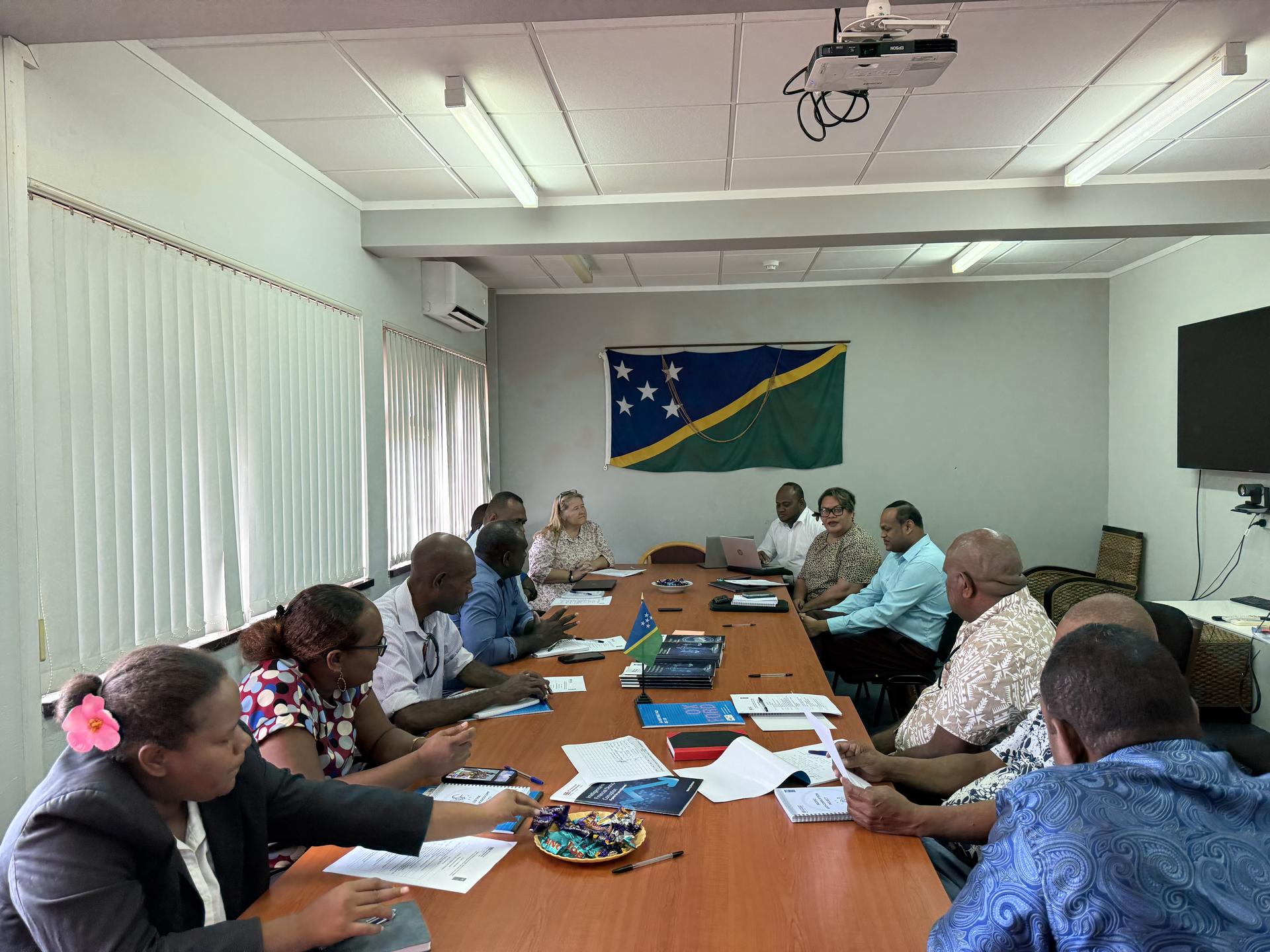 Group of people in a conference room discussing with a flag on the wall.