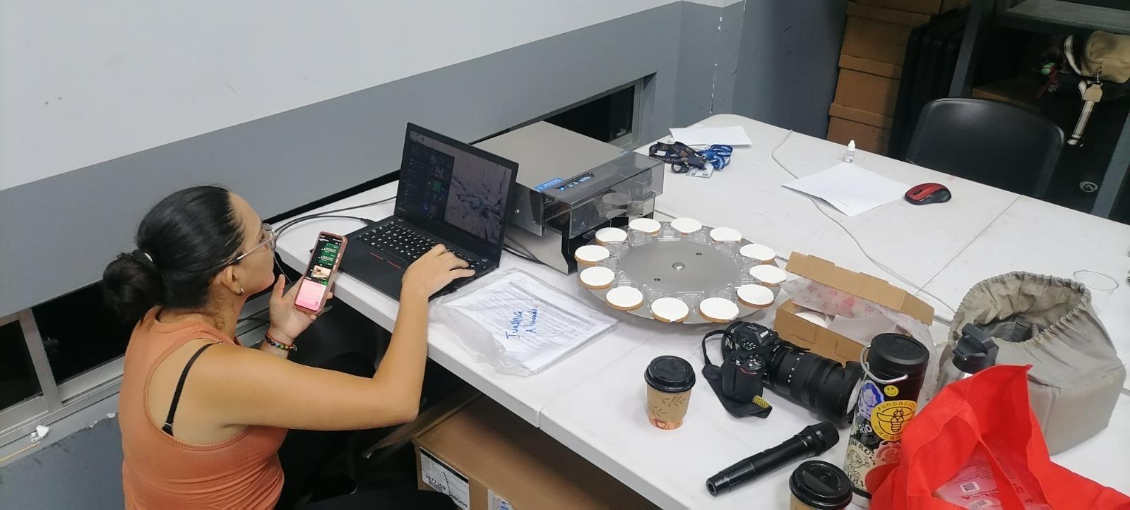 A person working on a laptop at a table with coffee, camera, and cupcakes.