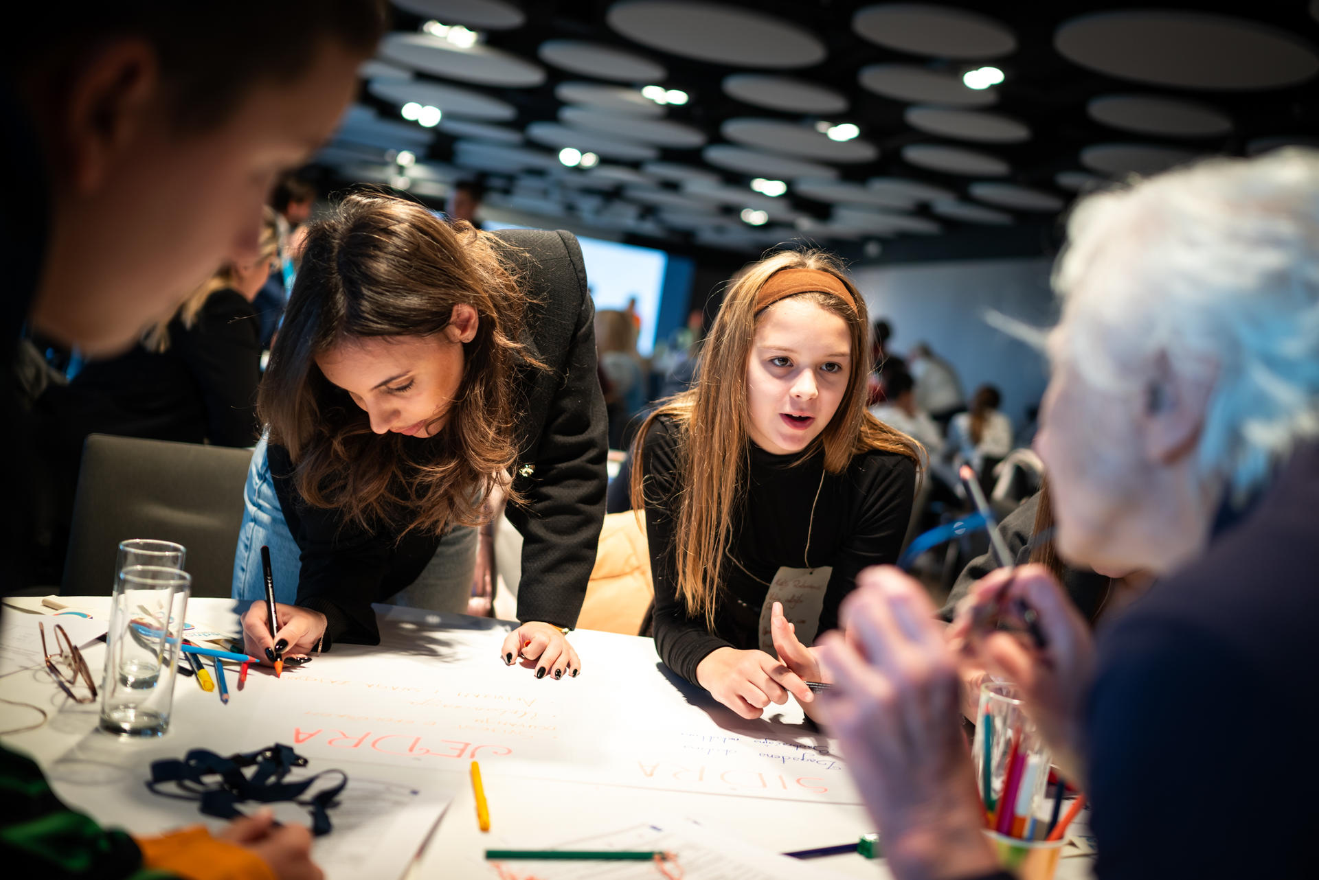 Group of people collaborating around a table, engaged in a discussion and writing on paper.