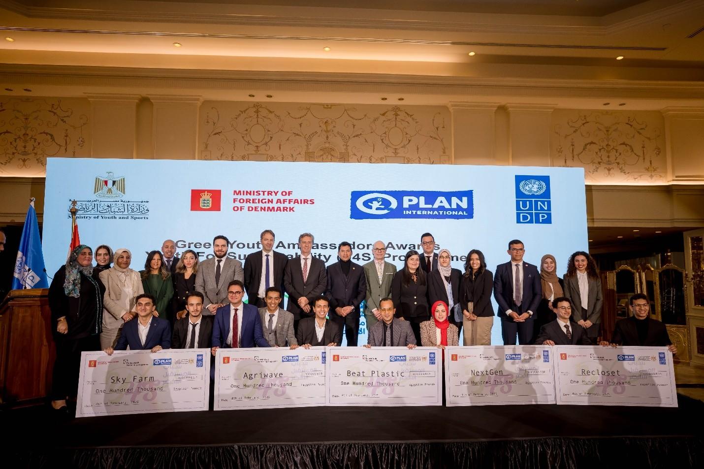 Group photo of people at a formal event with large checks and banners in the background.