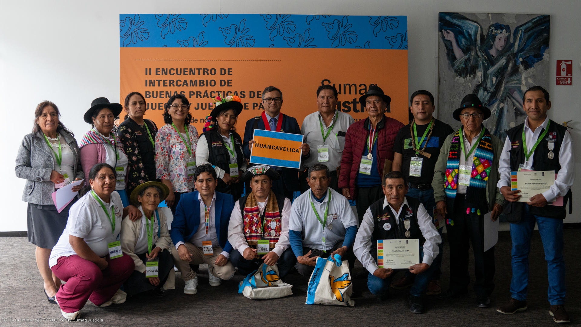 A diverse group of people posing together, some in traditional clothing, in a conference setting.