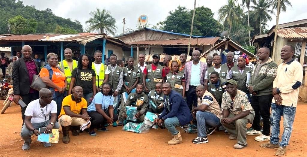 A diverse group of people posing together outdoors in a rural market setting.
