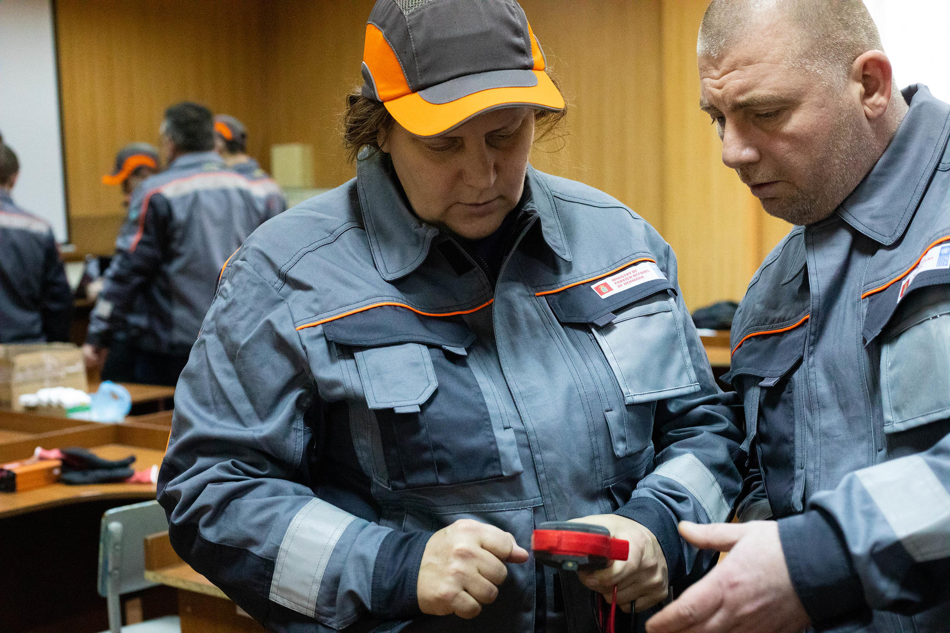 Two technicians in gray uniforms working on equipment in a workshop setting.