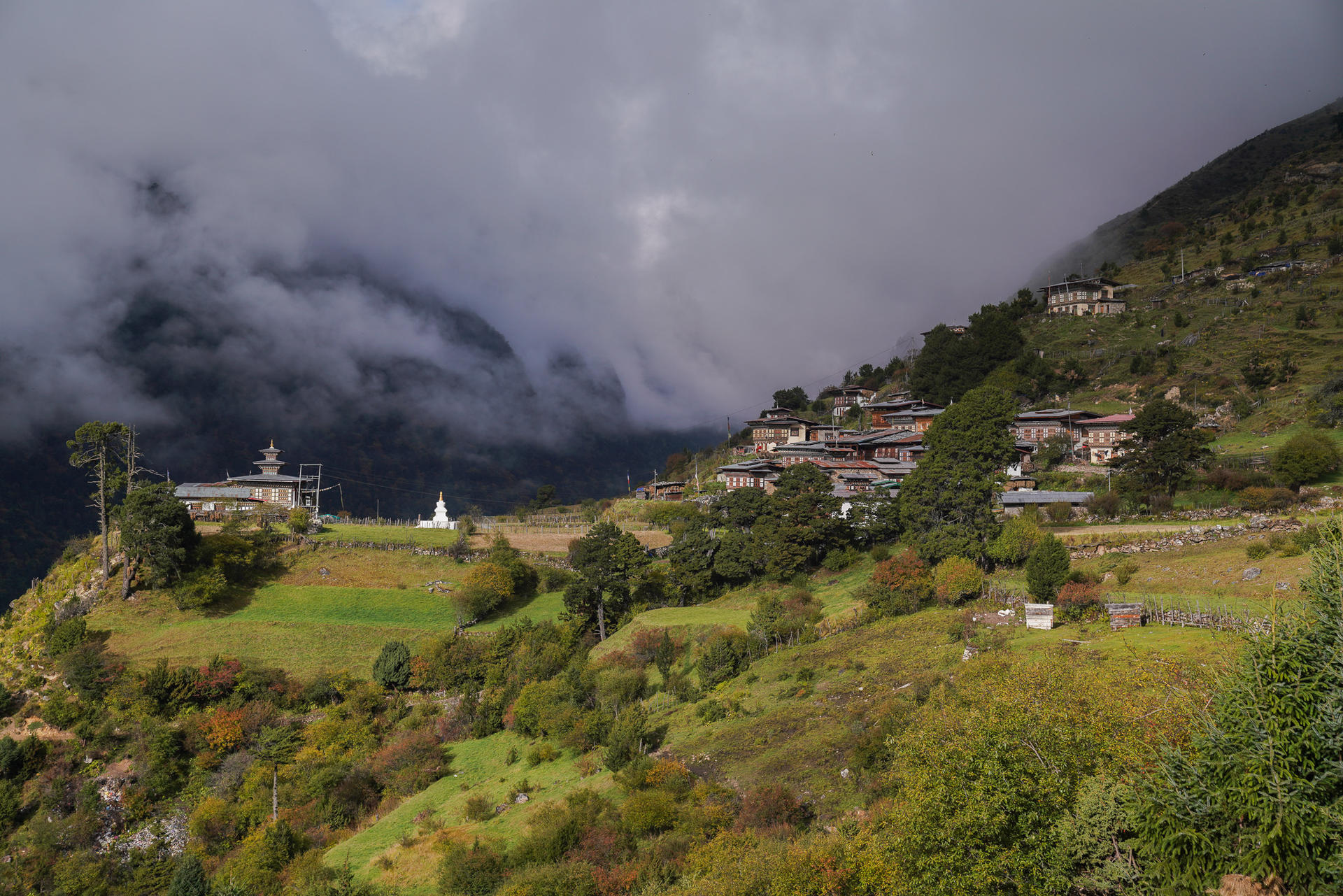 Lush green hills with a small village and cloudy mountains in the background.